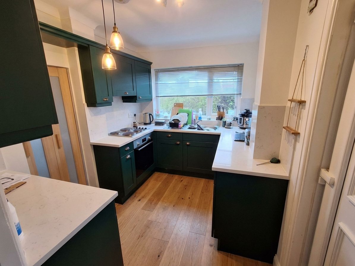 Forest green kitchen cabinets with white quartz, bronze hardware, light oak floors