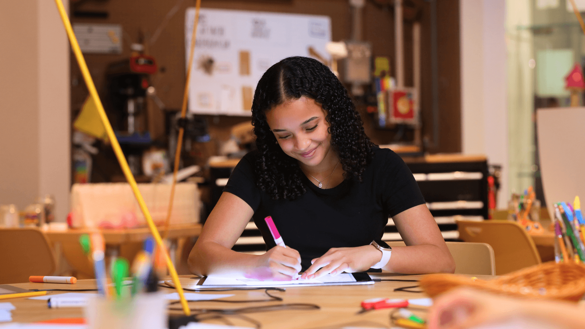 A girl smiles as she uses different markers to color her artwork.
