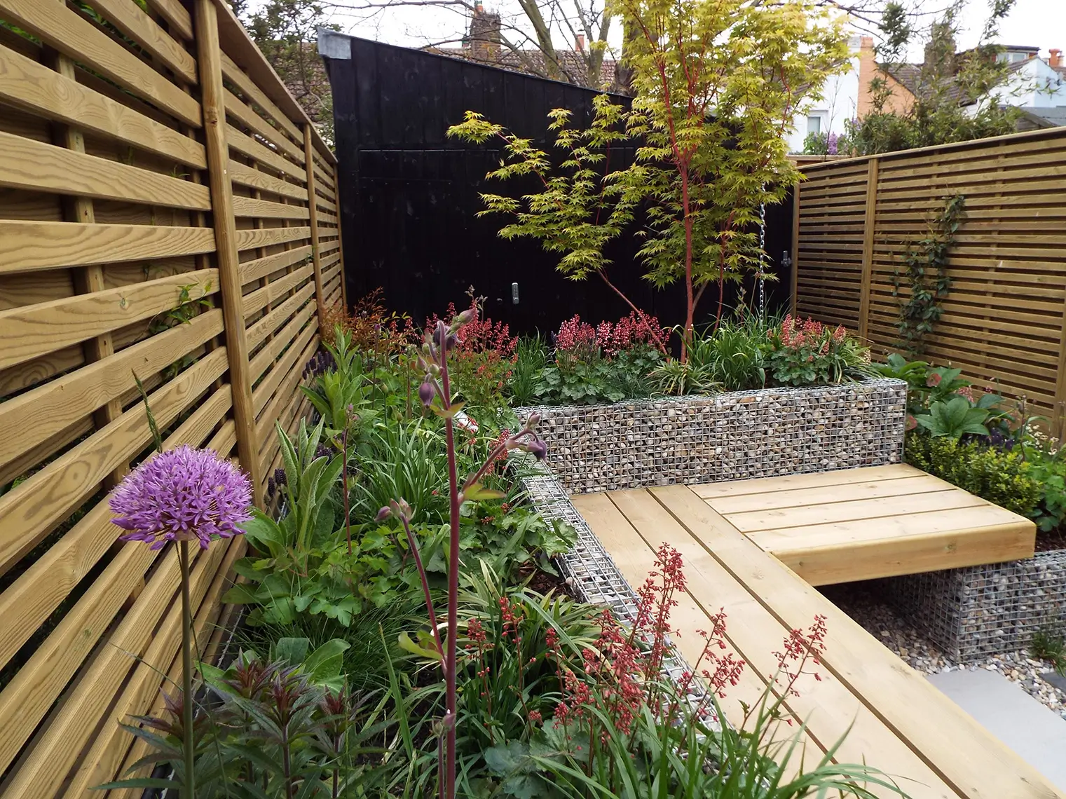 A cozy garden space featuring raised planters, wooden decking, and colorful flowers along wooden fencing.