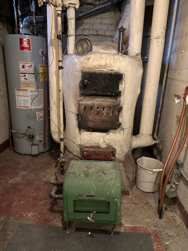 The image displays an old cast-iron boiler system and a modern water heater in a basement