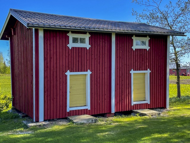 Ulkomaalattu punainen ulkorakennus Lappajärvellä, valkoiset nurkkalaudat ja keltaiset ikkunaluukut, huoliteltu piha-alue