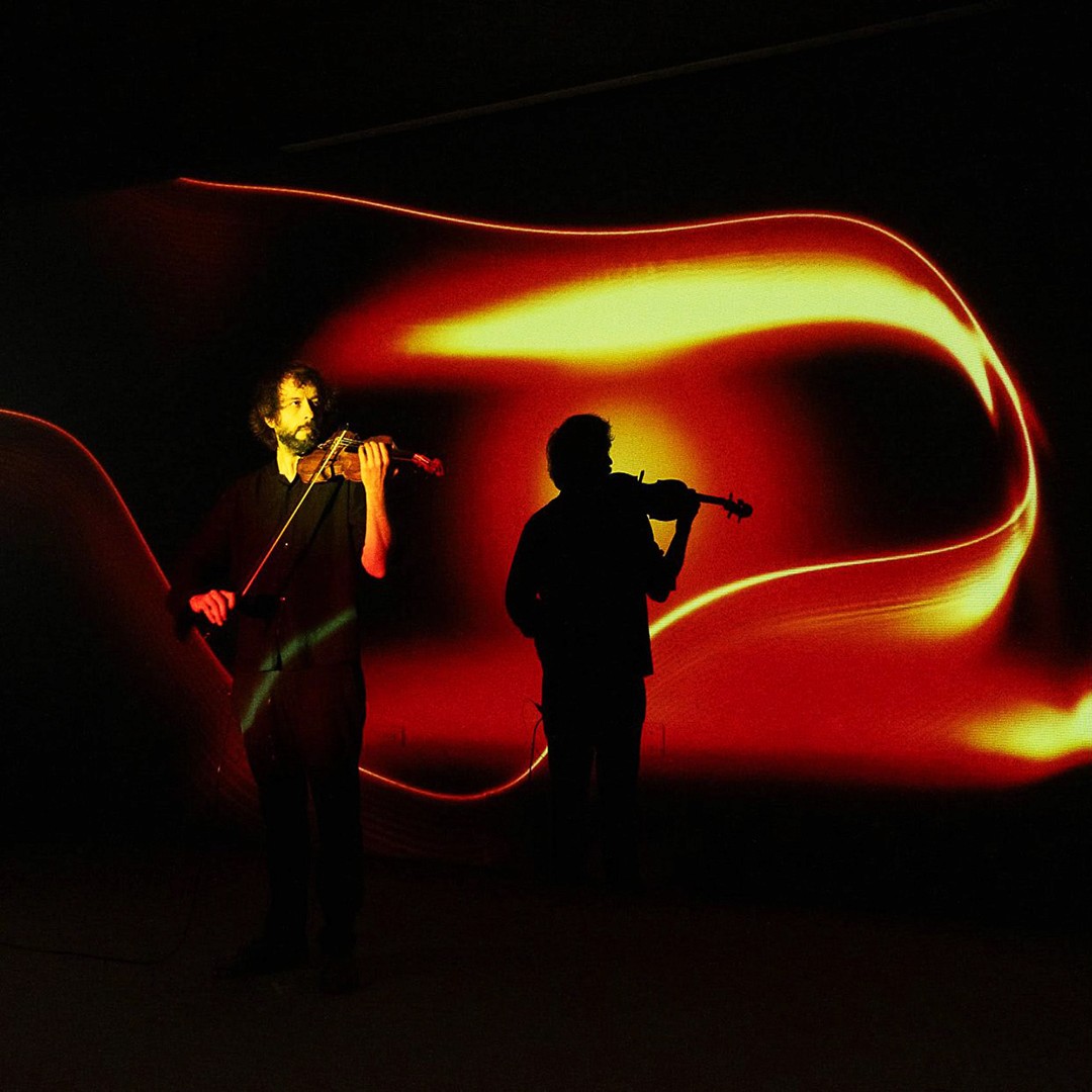 Man playing the violin with a projection of an abstract ochre-coloured organic form