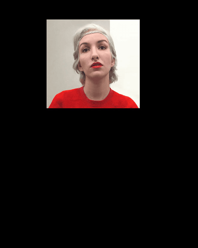 A woman with short gray hair and a silver headband wears a red sweater. She looks directly at the camera against a plain white background.