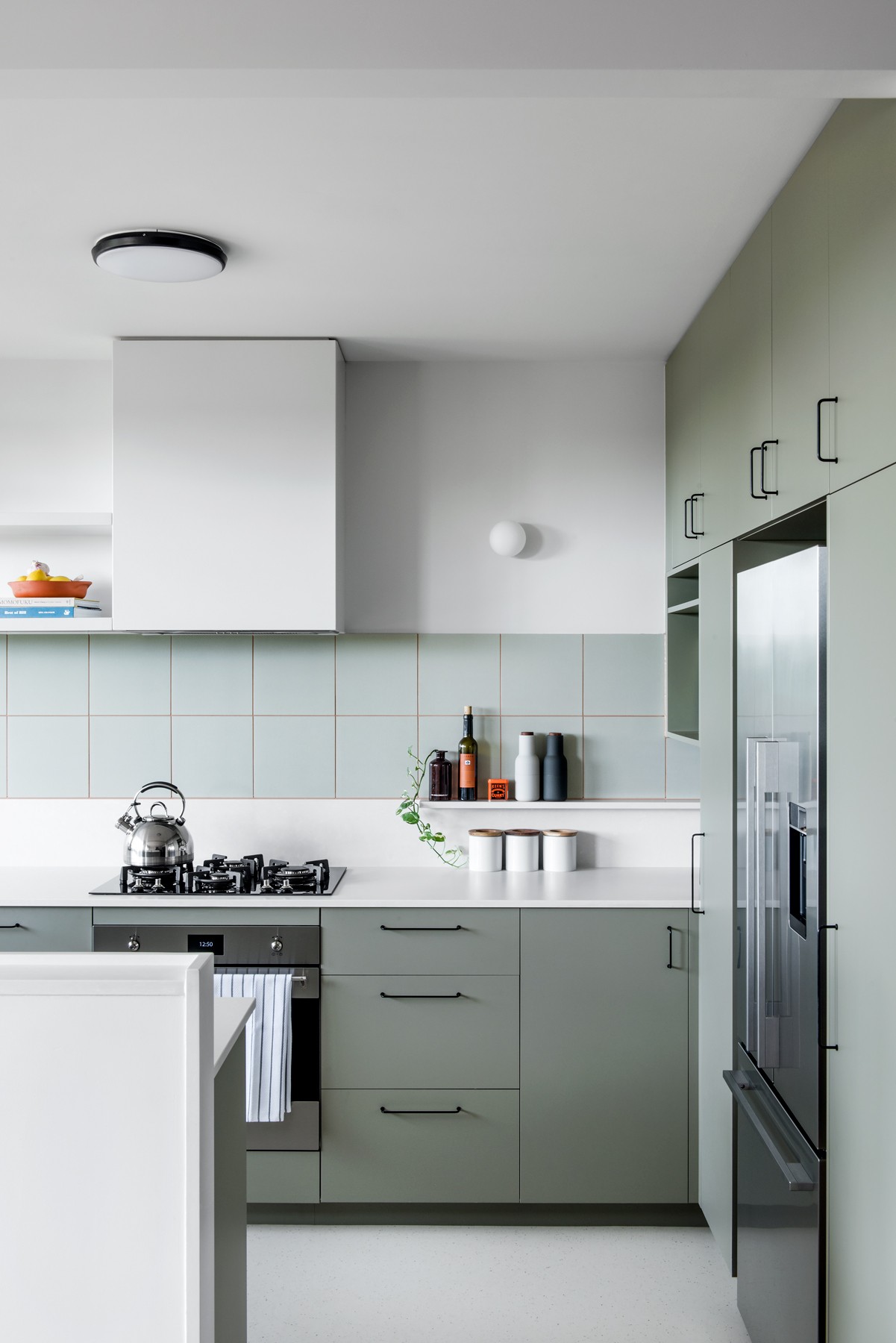 Wide kitchen view at Glenhaven, with muted green cabinetry, integrated appliances, and a light-filled layout anchored by a simple material palette.