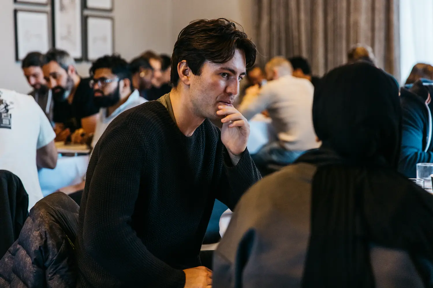 Person sitting and talking to another person in a busy room.