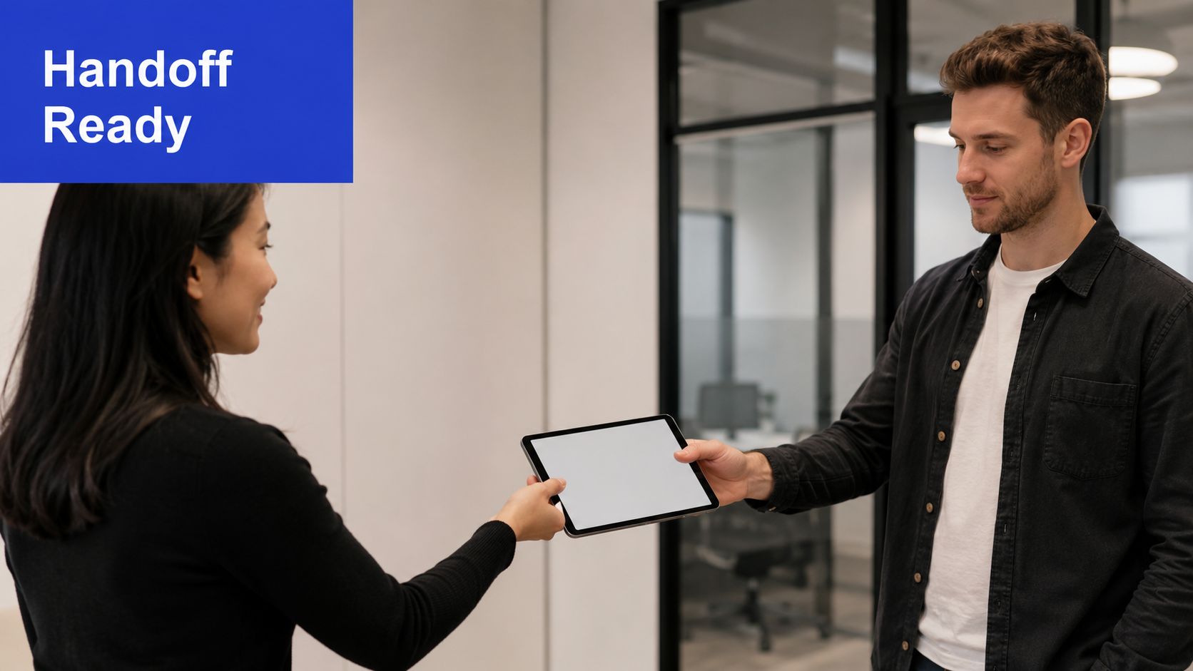 A professional woman passing a digital tablet to a man in a modern office environment.
