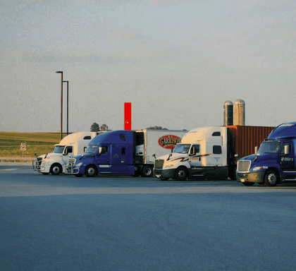 Row of semi-trucks parked at a rest area under an evening sky.