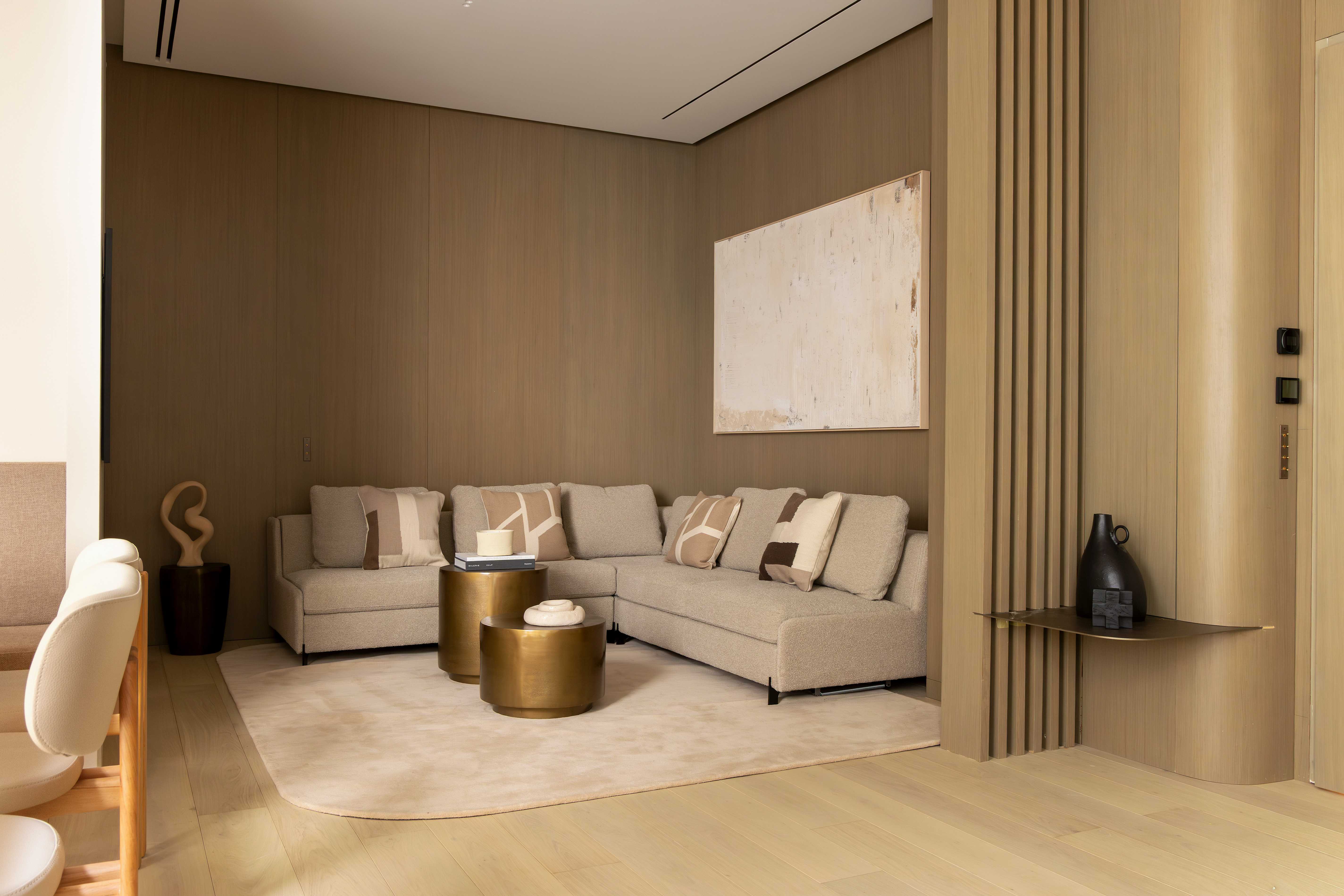 Salon vu de face avec canape d'angle beige, coussins, table doree, tableau abstrait et claustra en bois