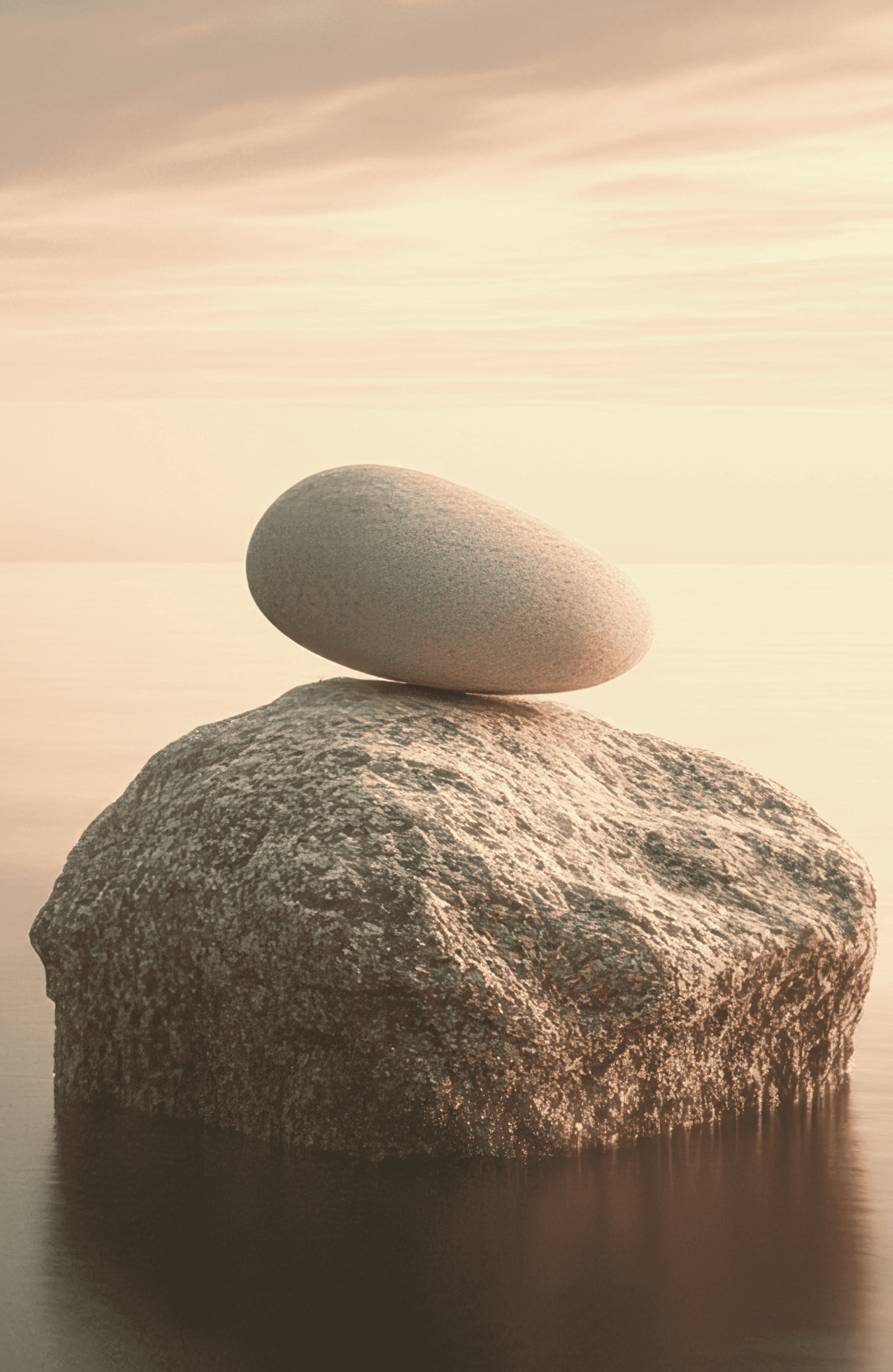 Smooth stone balanced on larger rock in calm water at sunset