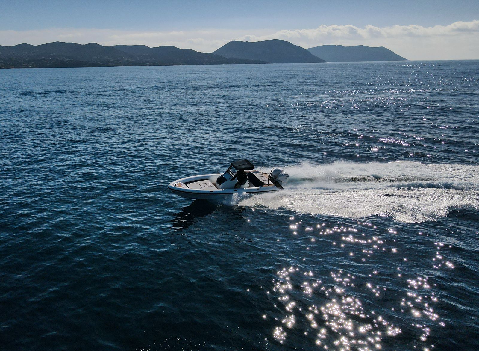 White Rock 36 speedboat with captain at helm cruising calm blue waters near Paros coastline with hills in background.