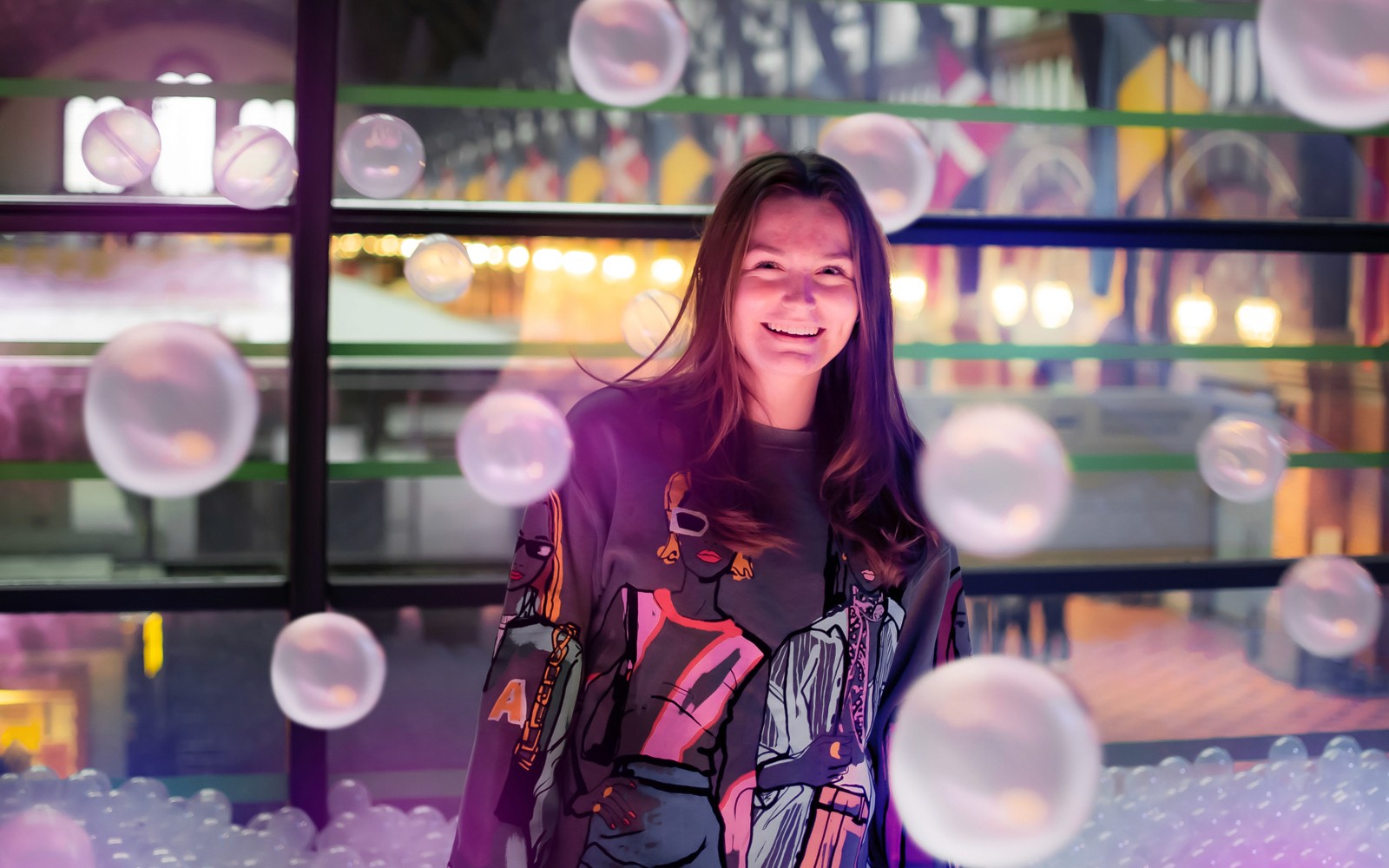 Egy személy mosolyog a koppenhágai The TUBE-ben, színes fényekkel és buborékokkal körülvéve.