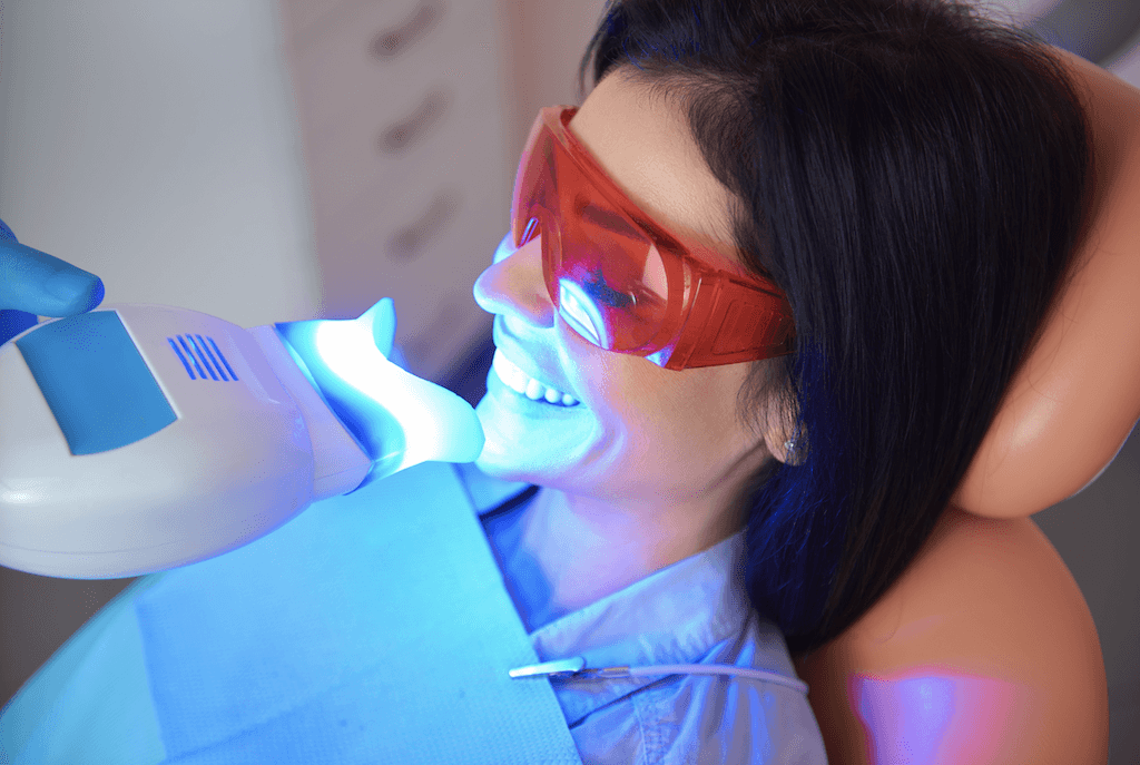 Photo of woman wearing protective red glasses underoing teeth whitening procedure