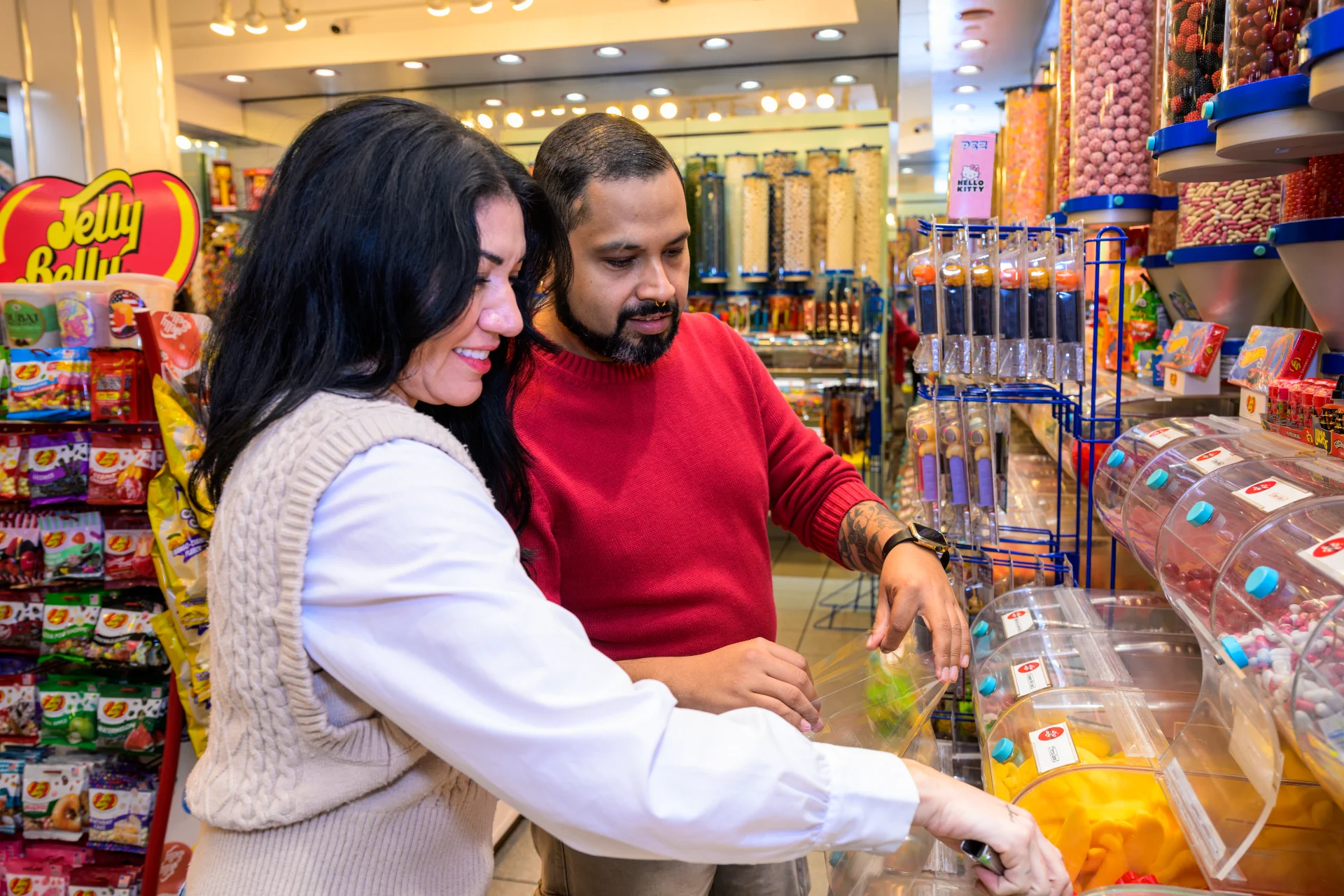 Couple filling a bag from the bulk candy bins at Candy Verse, with Jelly Belly displays behind them