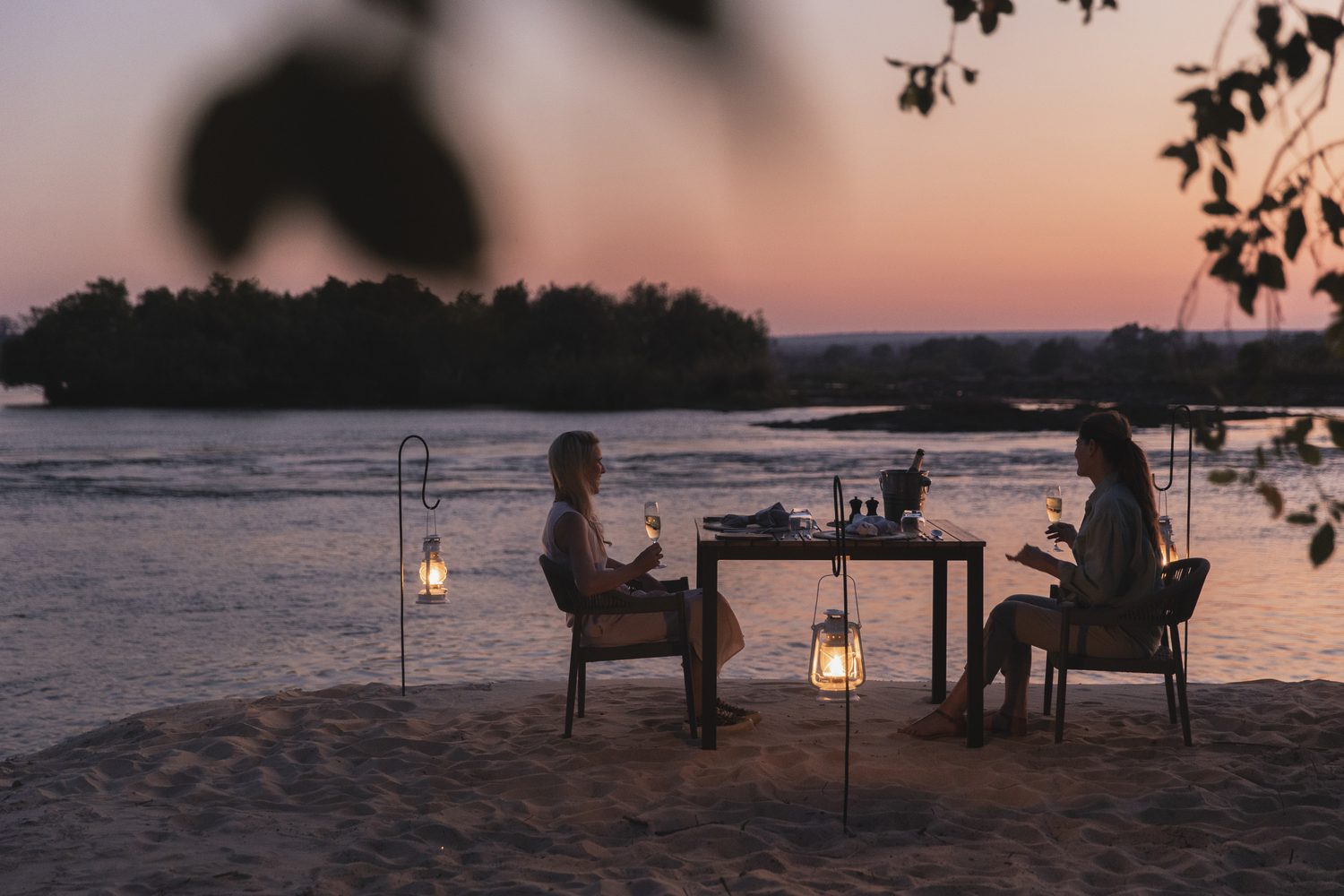 A lantern-lit dinner for two on the riverbank at dusk