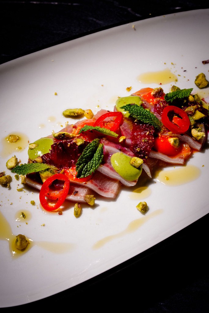 Colorful seafood dish topped with sliced peppers, mint leaves, and pistachios on a white plate.