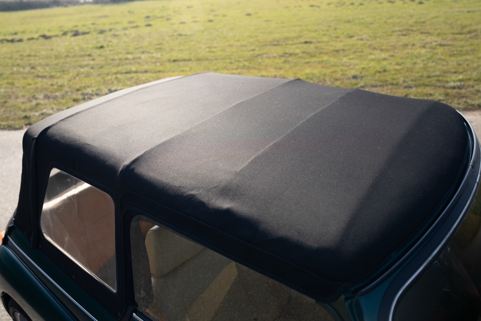 A close-up view of a black convertible car roof with sunlight reflecting off its surface.
