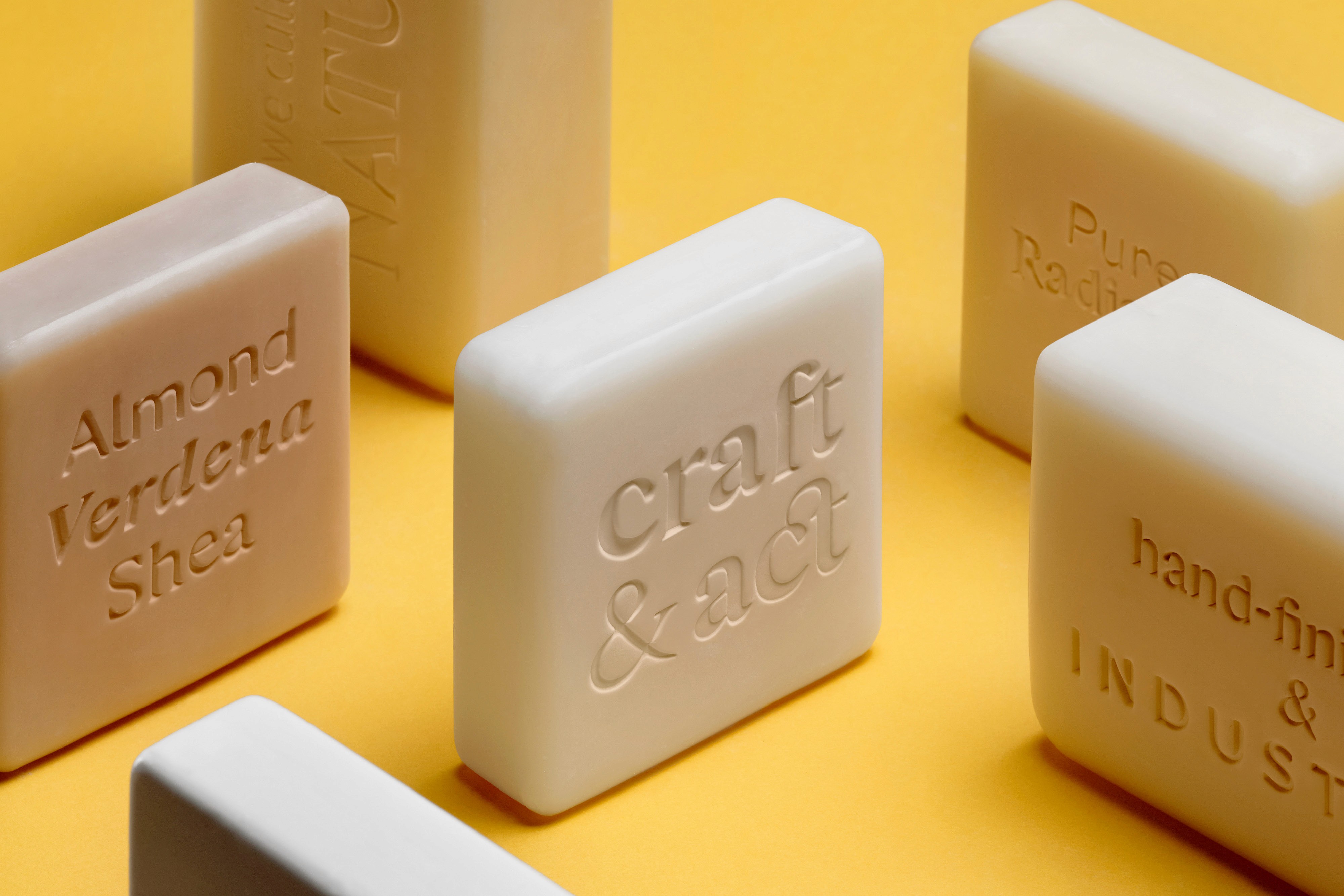 A collection of minimalist soap bars in various colors, arranged on a bright yellow background.