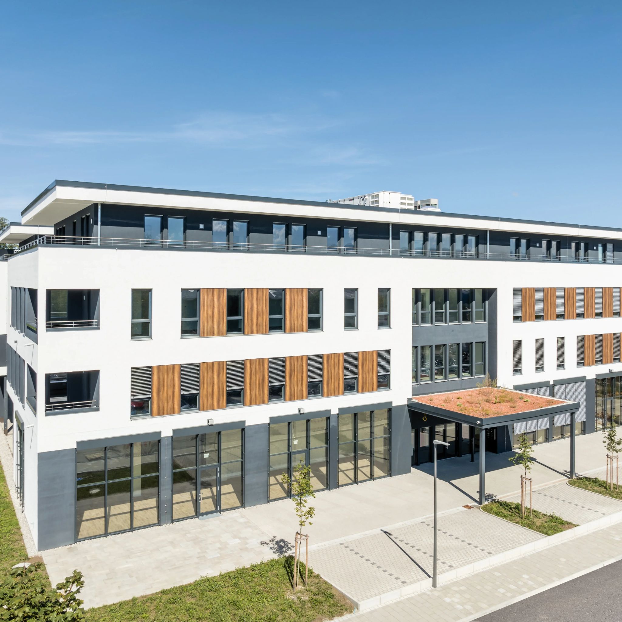Modernes Bürogebäude mit weißer Fassade, Holzapplikationen und großen Glasflächen, unter einem blauen Himmel.