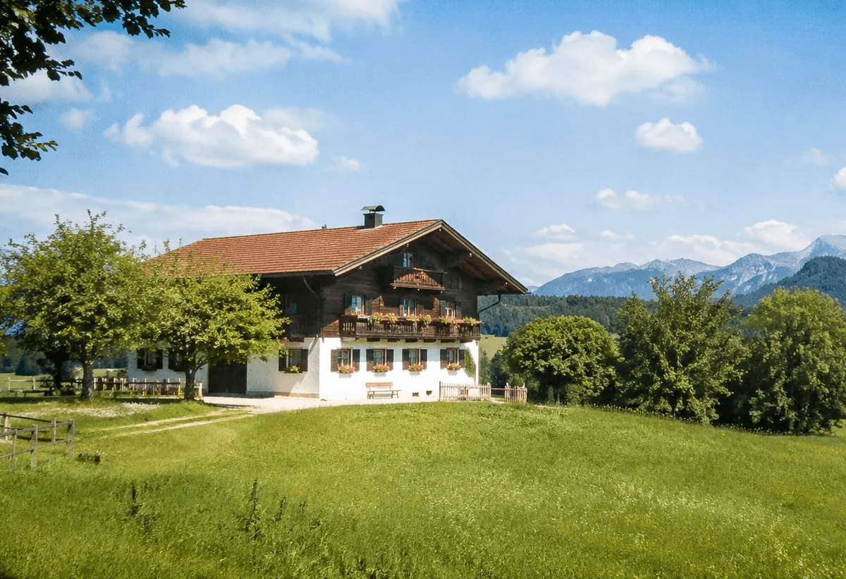 Helle bayerische Landschaft mit Bauernhaus, grünen Wiesen und Alpen im Hintergrund