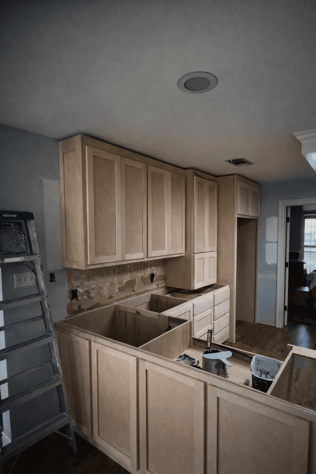 A modern, luxury beachfront villa with large glass windows and balconies overlooks a rocky shoreline, surrounded by palm trees at sunset.