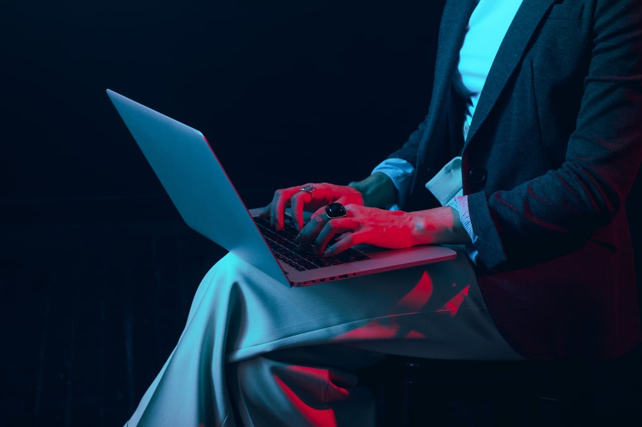 A woman's hands typing on a laptop, with a red light shining on them.