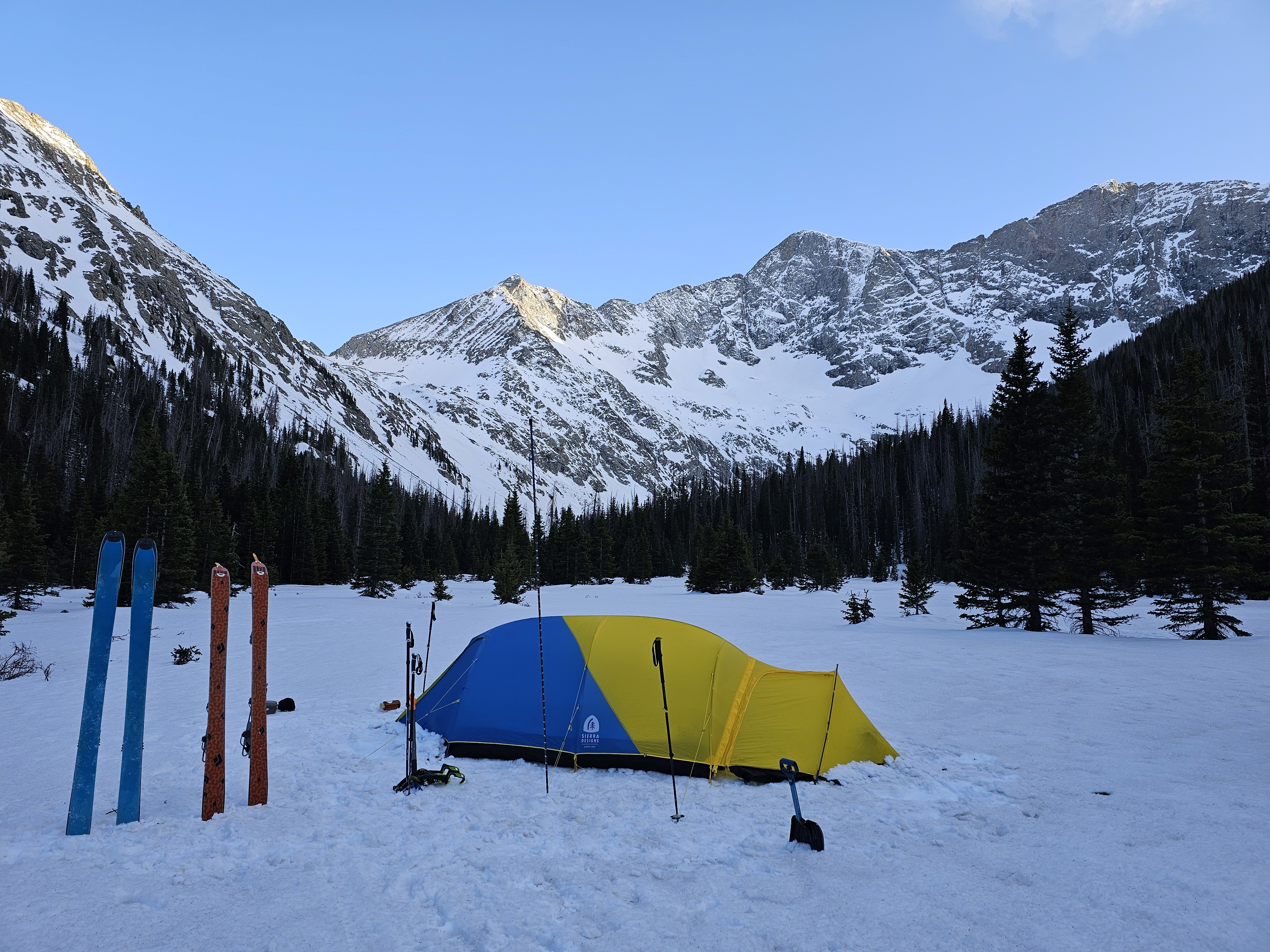 A tent and skis sit in the valley on the snow below Blanca Peak