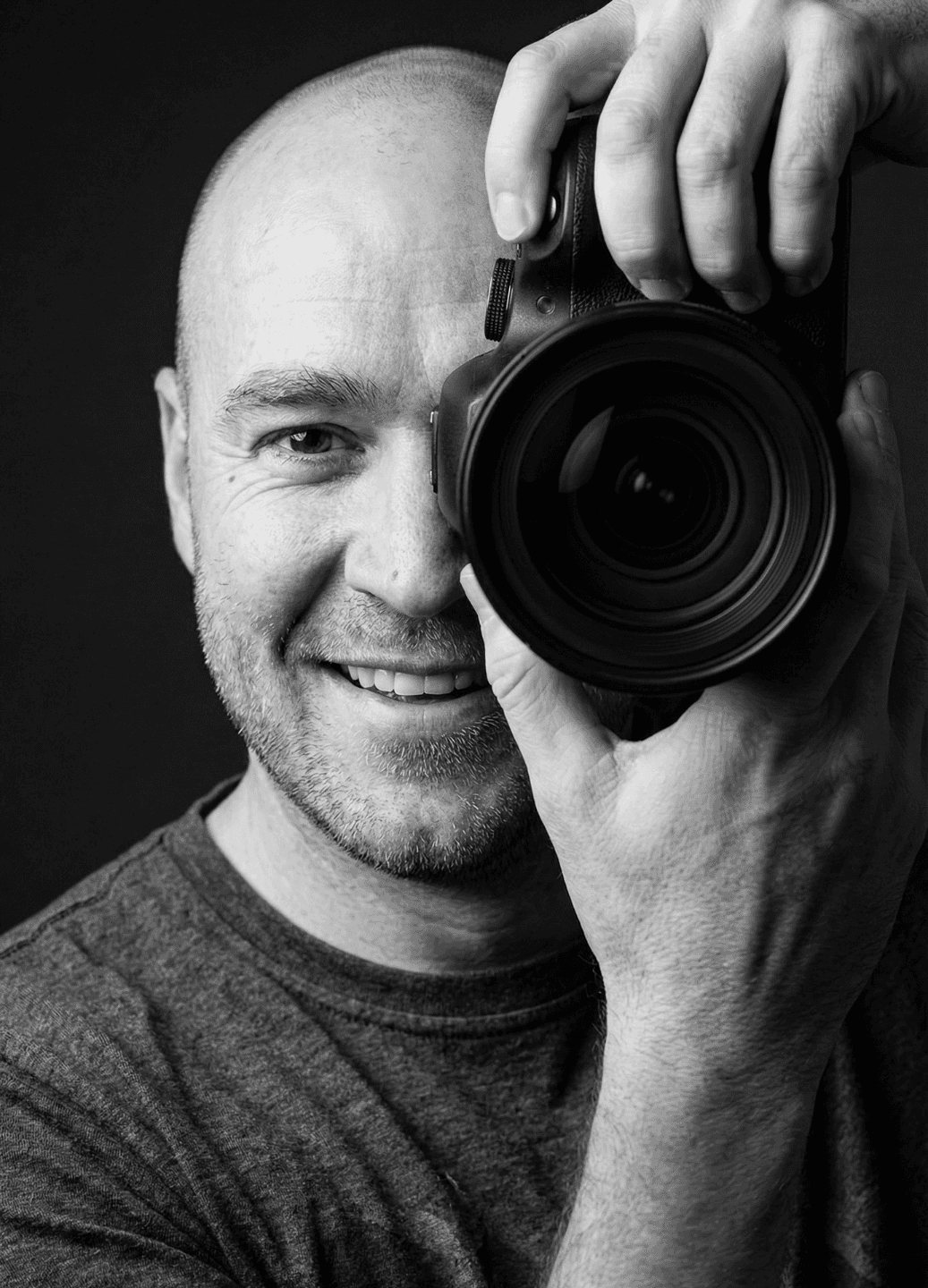 Smiling photographer holding a camera to his eye.