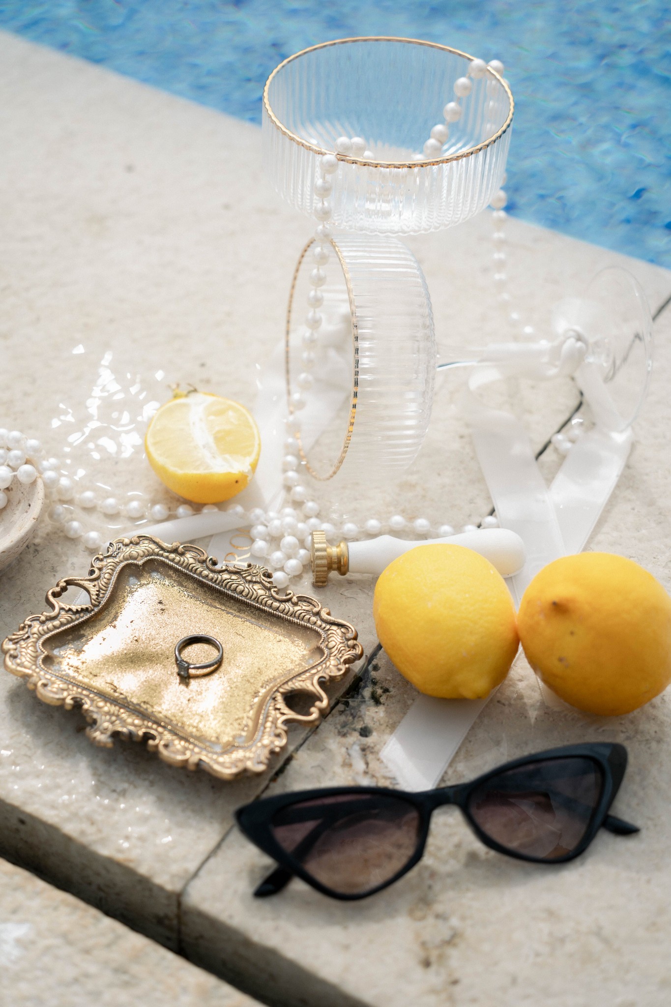 Kreatives Flatlay-Foto des Eherings auf einem goldenen Tablett mit Zitronen, Perlen und Parfum, detailverliebt arrangiert für die Hochzeitsfotografie