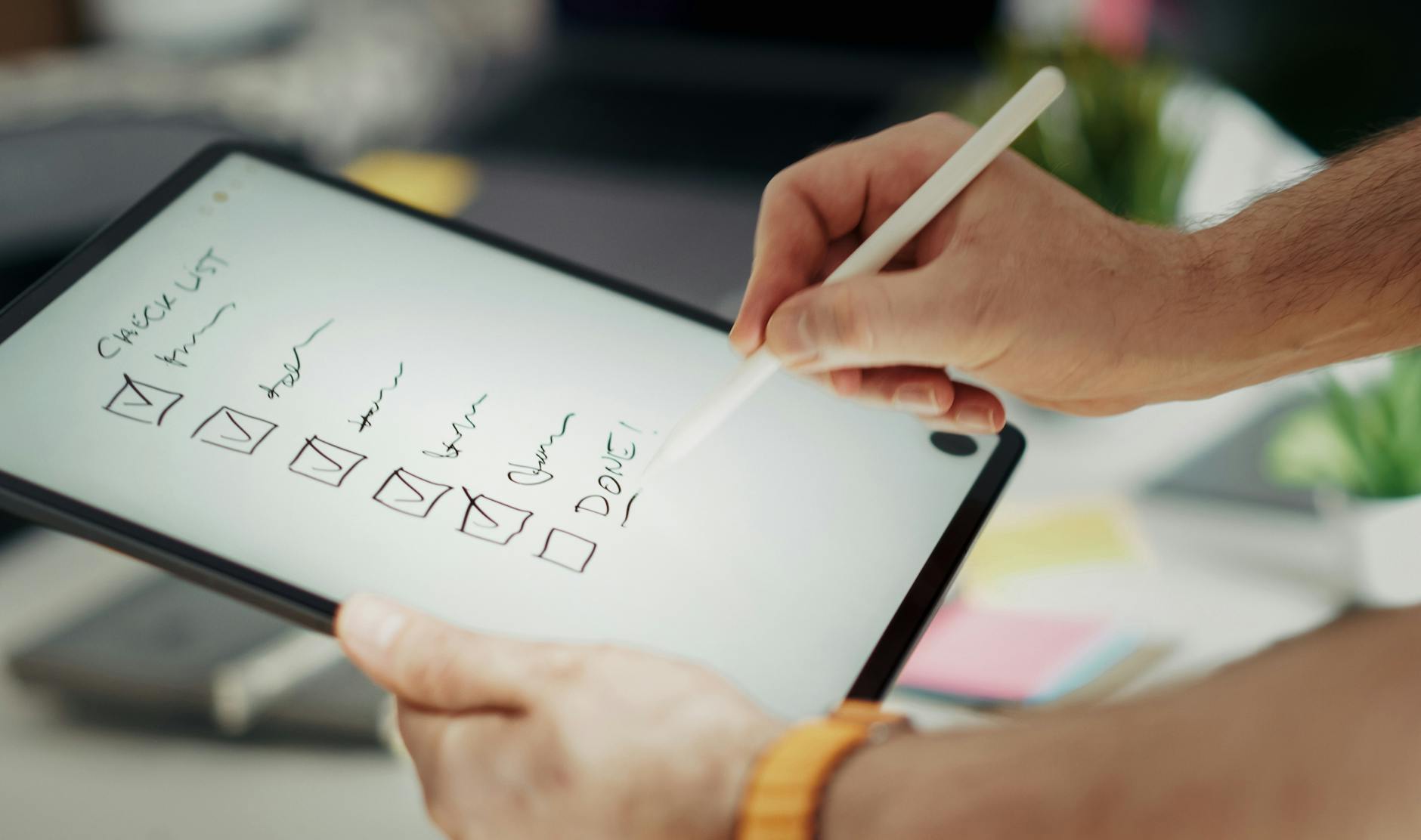 A close-up of a person's hand checking off items on a printed to-do list next to a tablet showing free math lesson plans.