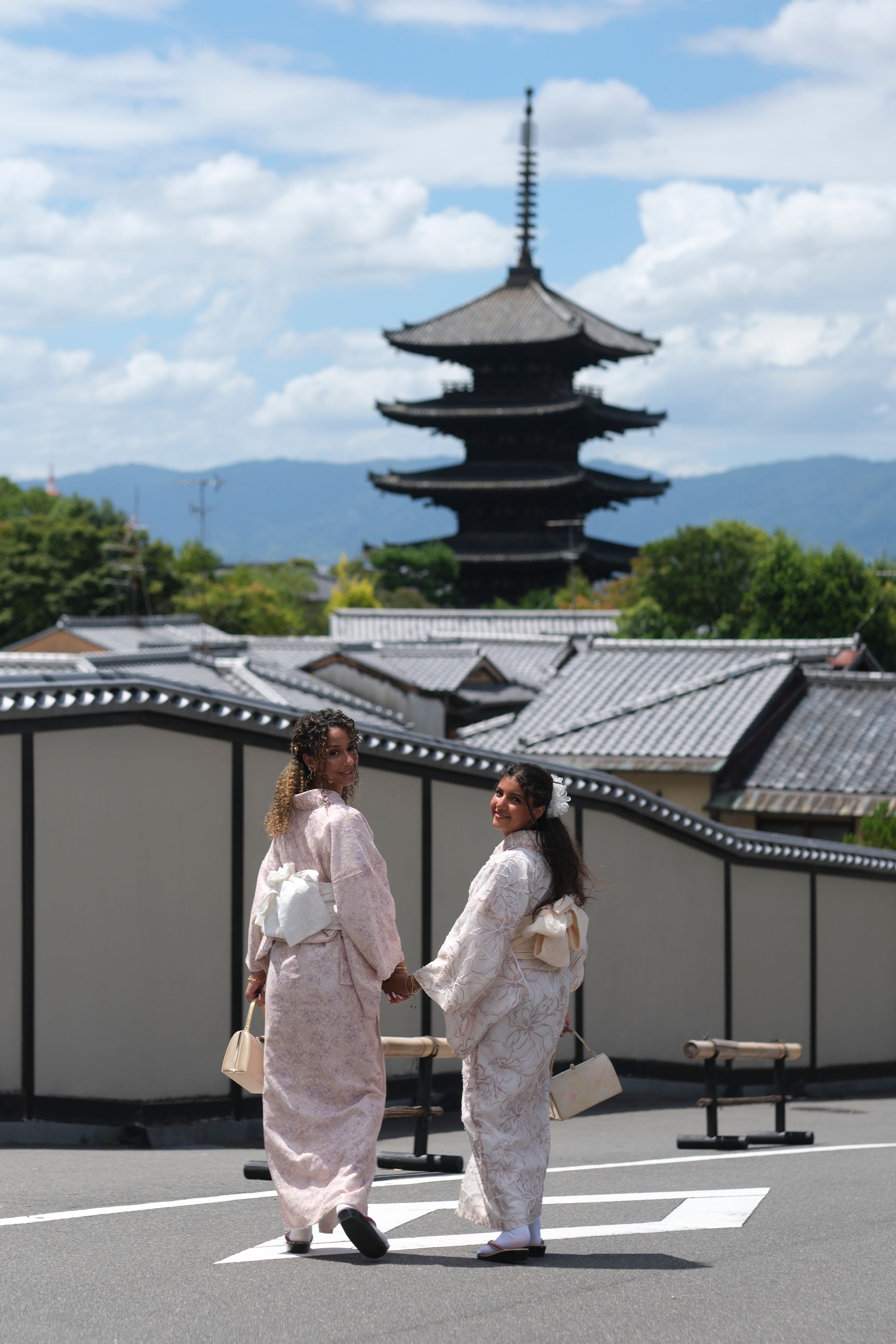 Two young women walking together in Kyoto with a pagoda in the background