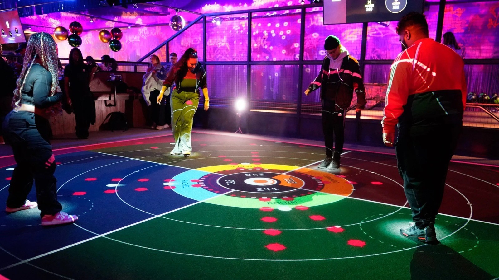 Group of guests playing together on a large digitally projected interactive floor inside a competitive socialising venue.