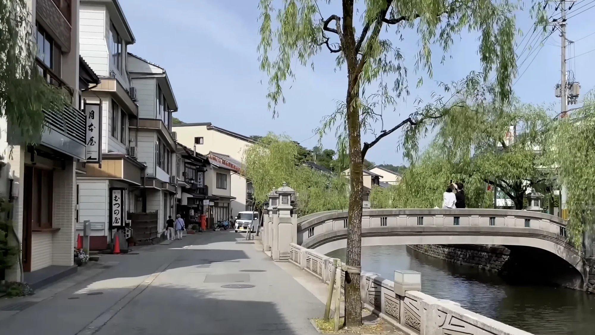 An arched stone bridge over the Kinosaki canal framed by full summer willow.