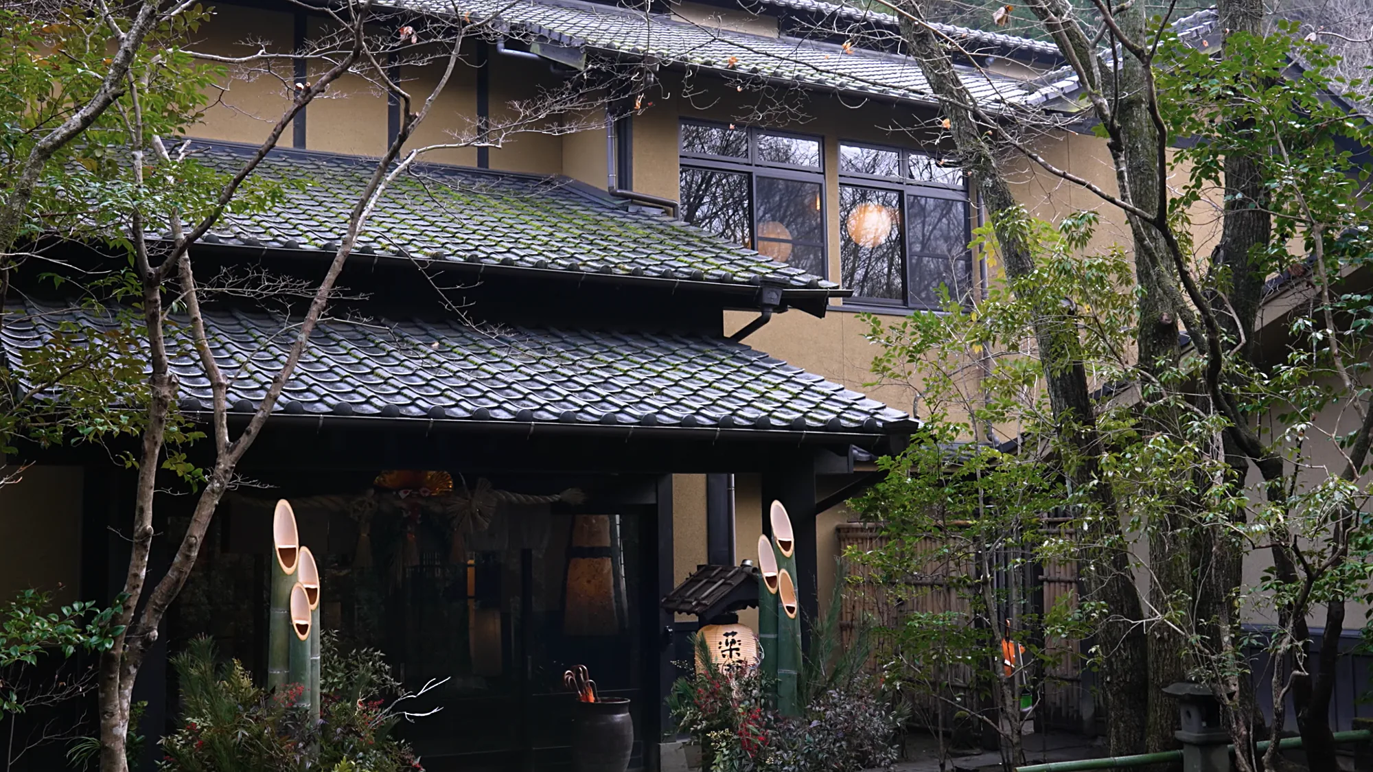 A tiled-roof inn entrance at Kurokawa Onsen among trees, lanterns hanging at the door