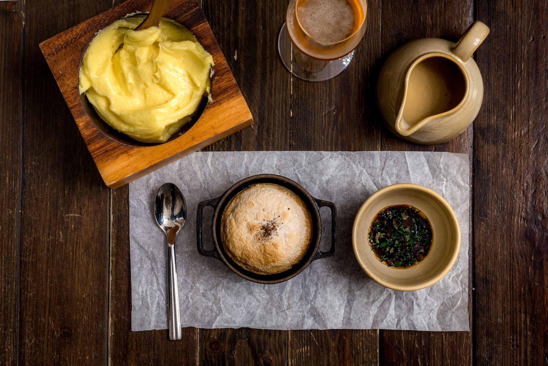 Top-down view of a rustic wooden table set with a large pastry, a cup of coffee with foam, and a small bowl of tea.