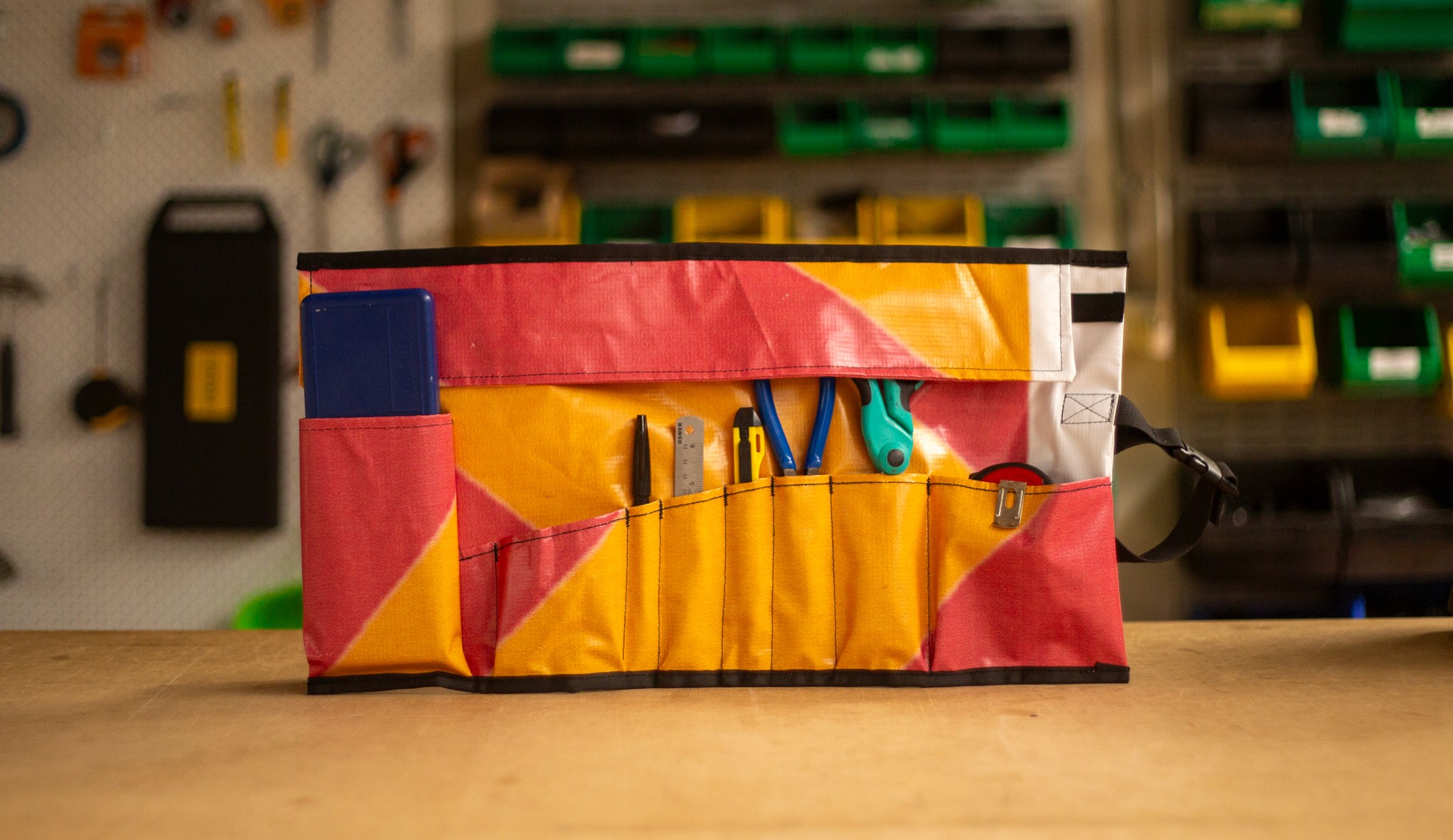 Upcycled tool roll made from colorful outdoor advertising banner, displaying neatly organized hand tools.
