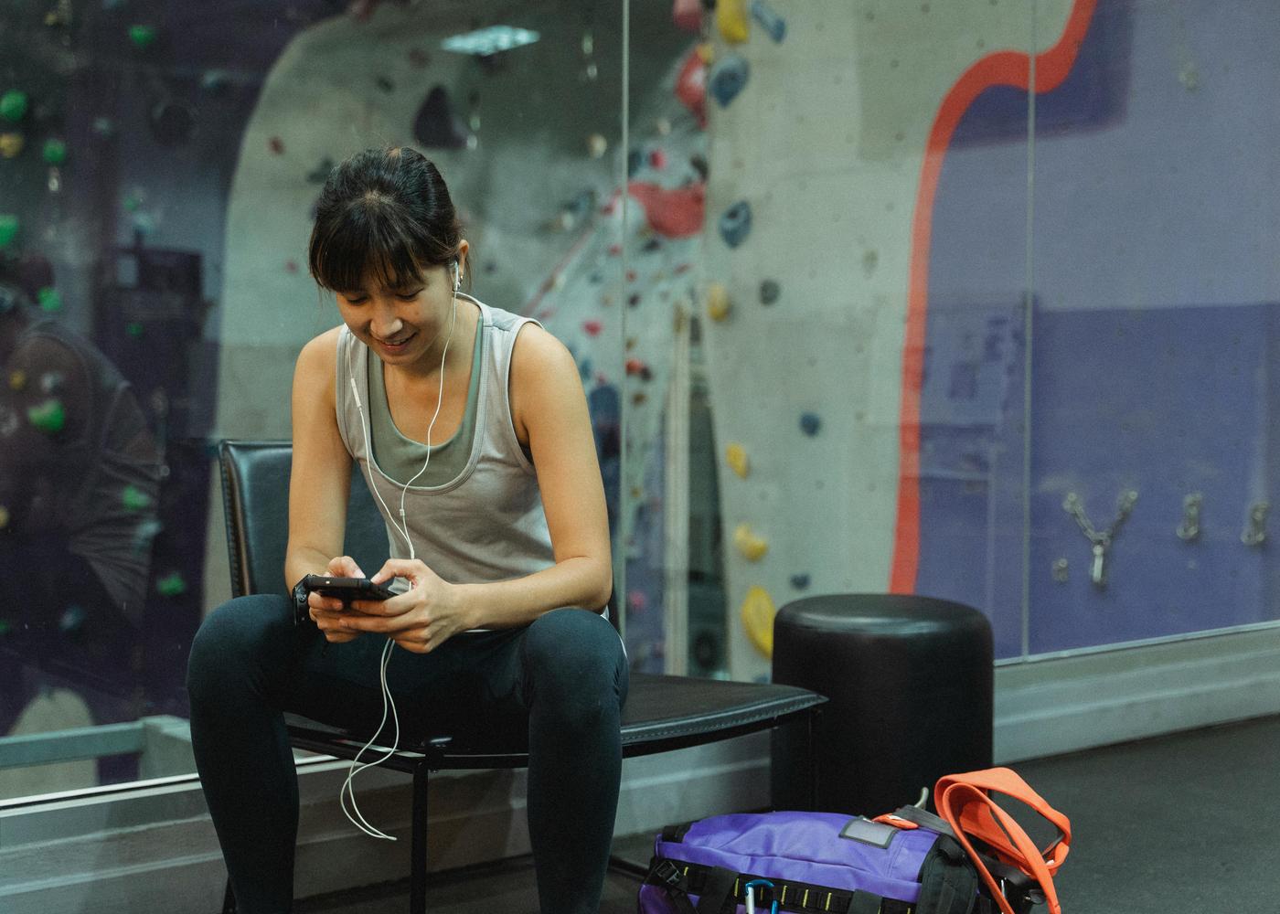 Happy woman in gym sitting on chair looking at phone