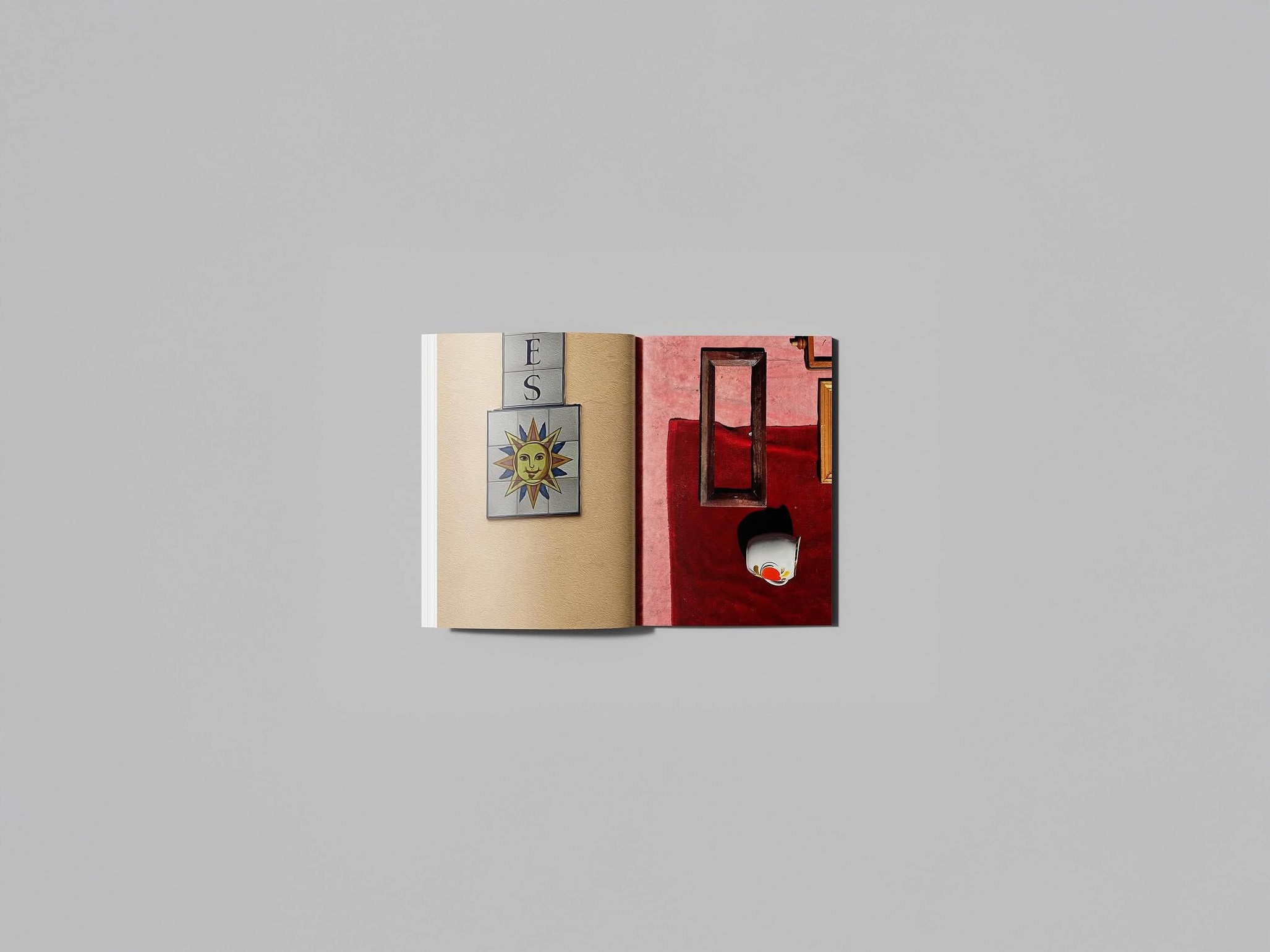 A two-page spread from an art book. On the left, a textured beige page features a collage of a sun face and letters spelling “ES.” On the right, a red velvet background holds an empty wooden frame and a white cup with a peach motif, suggesting absence, memory, and symbolic fragments.