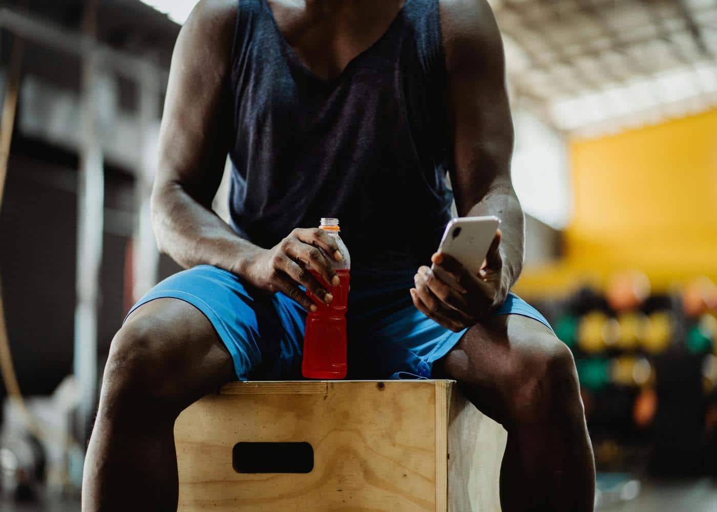Man sitting in gym while holding a red drink and looking at smartphone