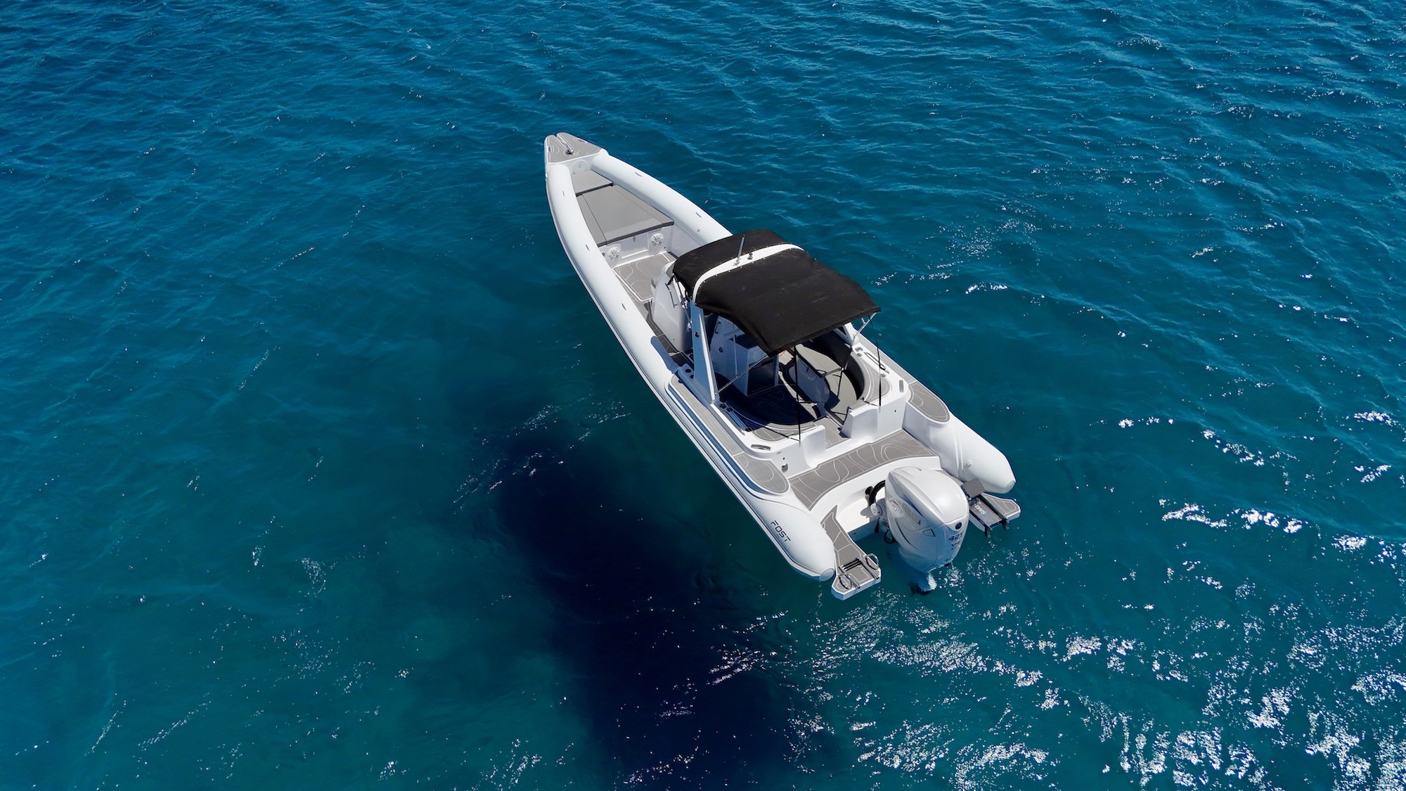 White Fost Matrix 32 rigid inflatable boat with central console and canopy anchored in crystal-clear turquoise waters.