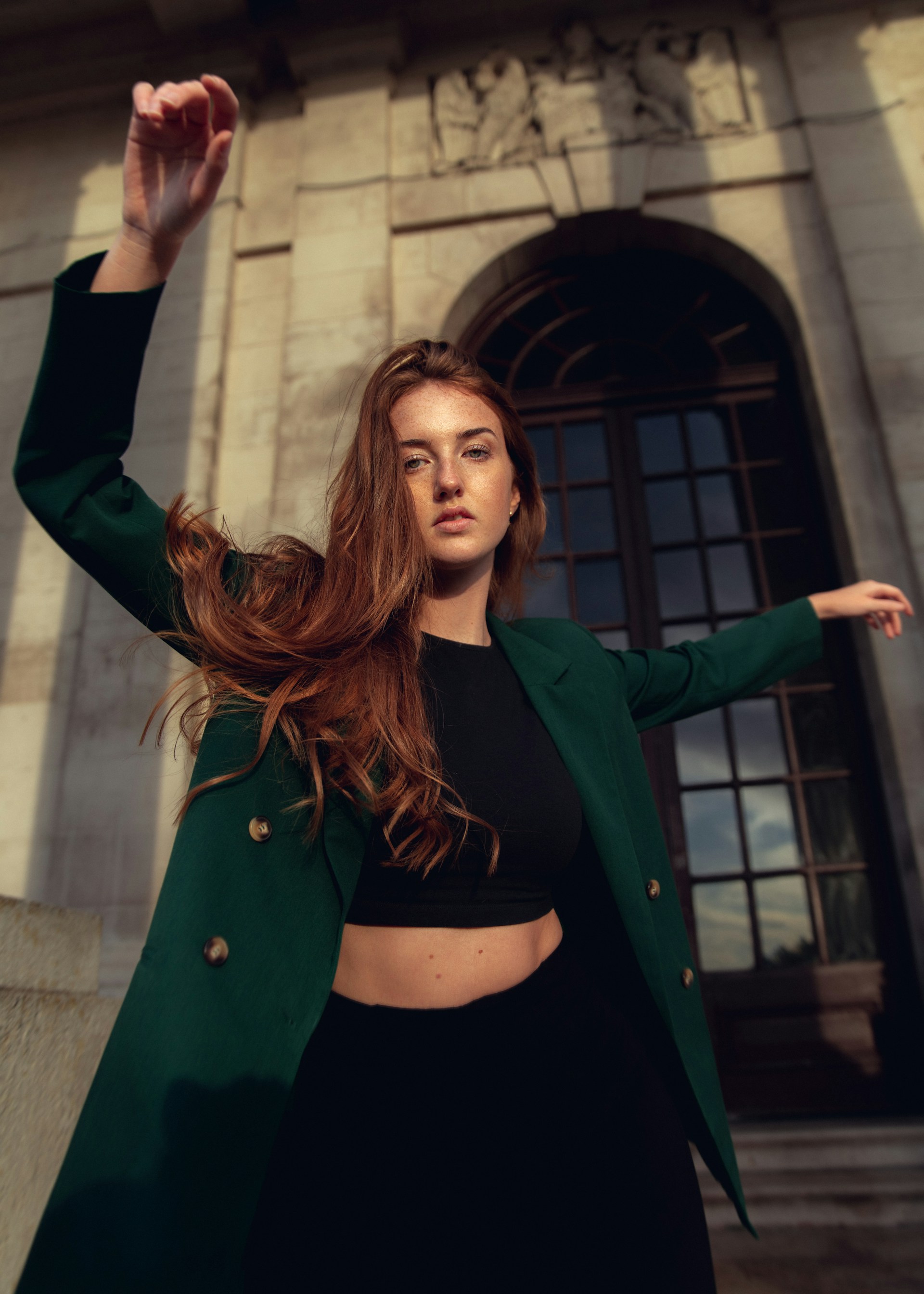 A portrait of a person with short natural hair wearing a black and red paisley bandana tied around their neck. They are wearing a black cardigan over a white top and looking directly at the camera with a neutral expression.