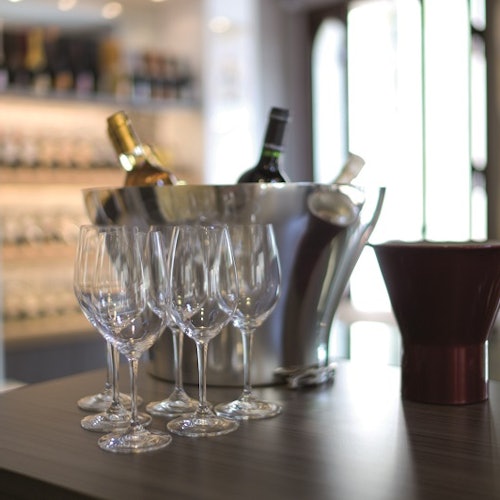 Champagne bottles in an ice bucket, six empty wine glasses, and a decanter on a countertop in a wine store.