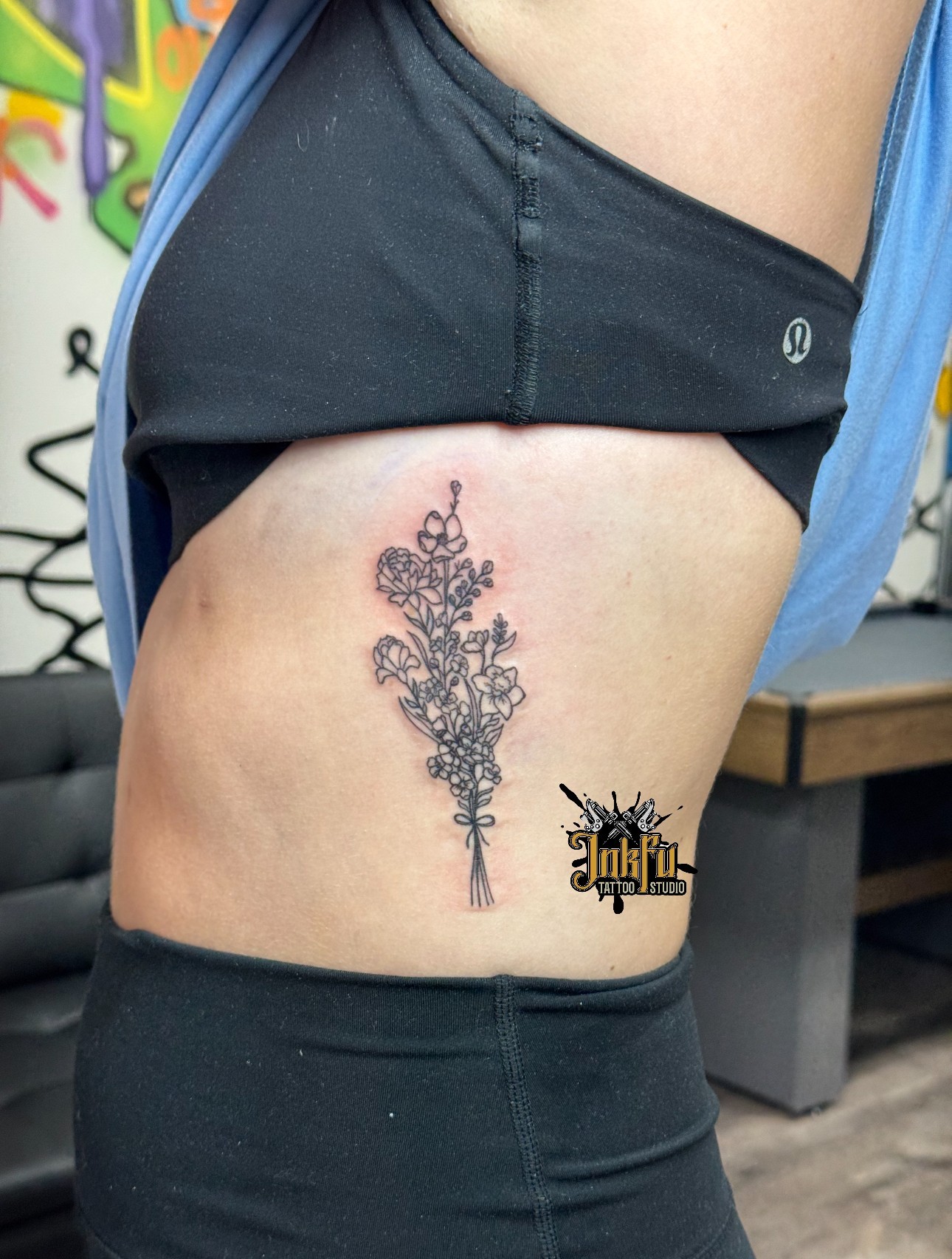 Fine line black outline botanical bouquet on the ribs, by Meer Rich