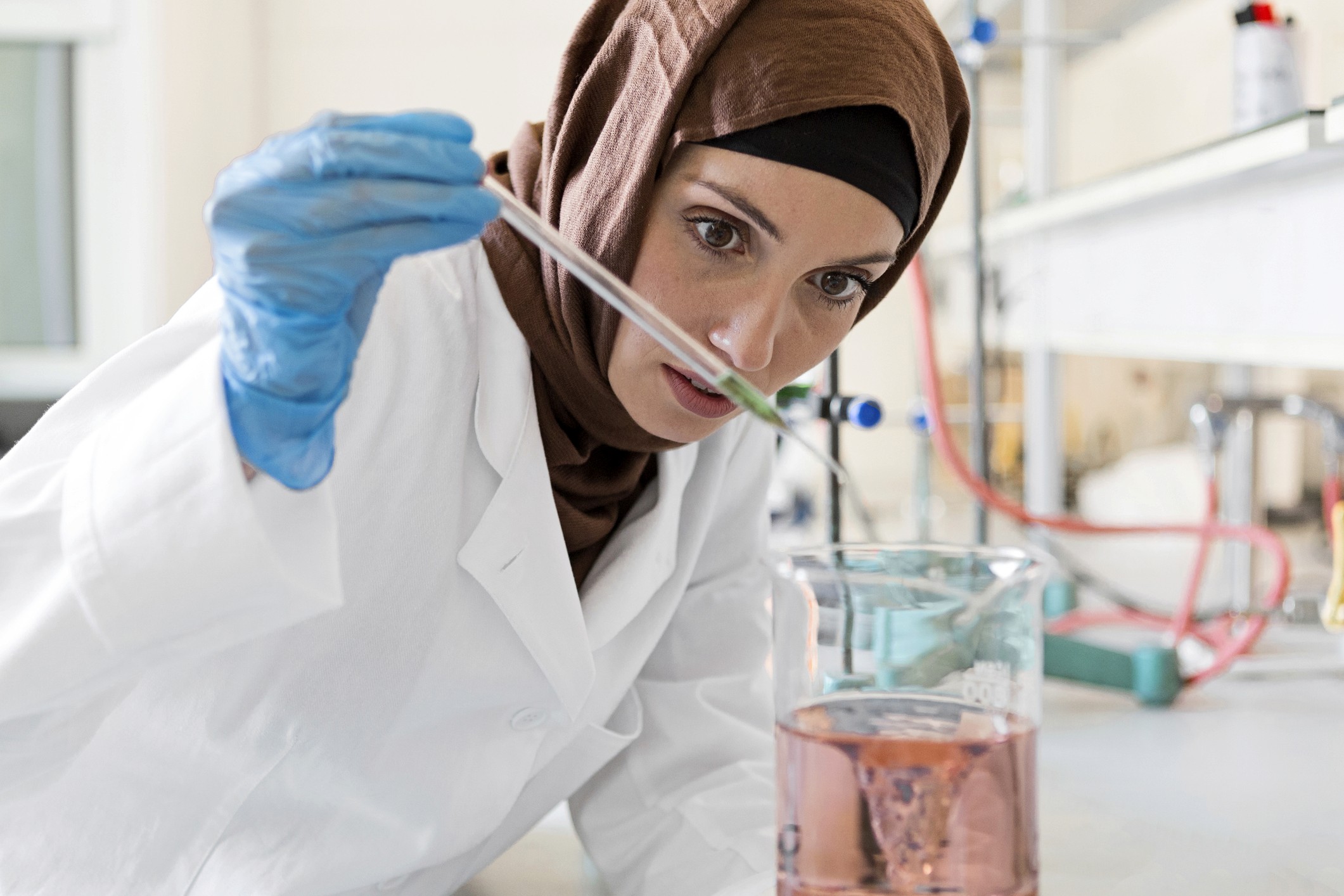 Confident female scientist standing with arms crossed in a cutting-edge laboratory filled with advanced scientific equipment.