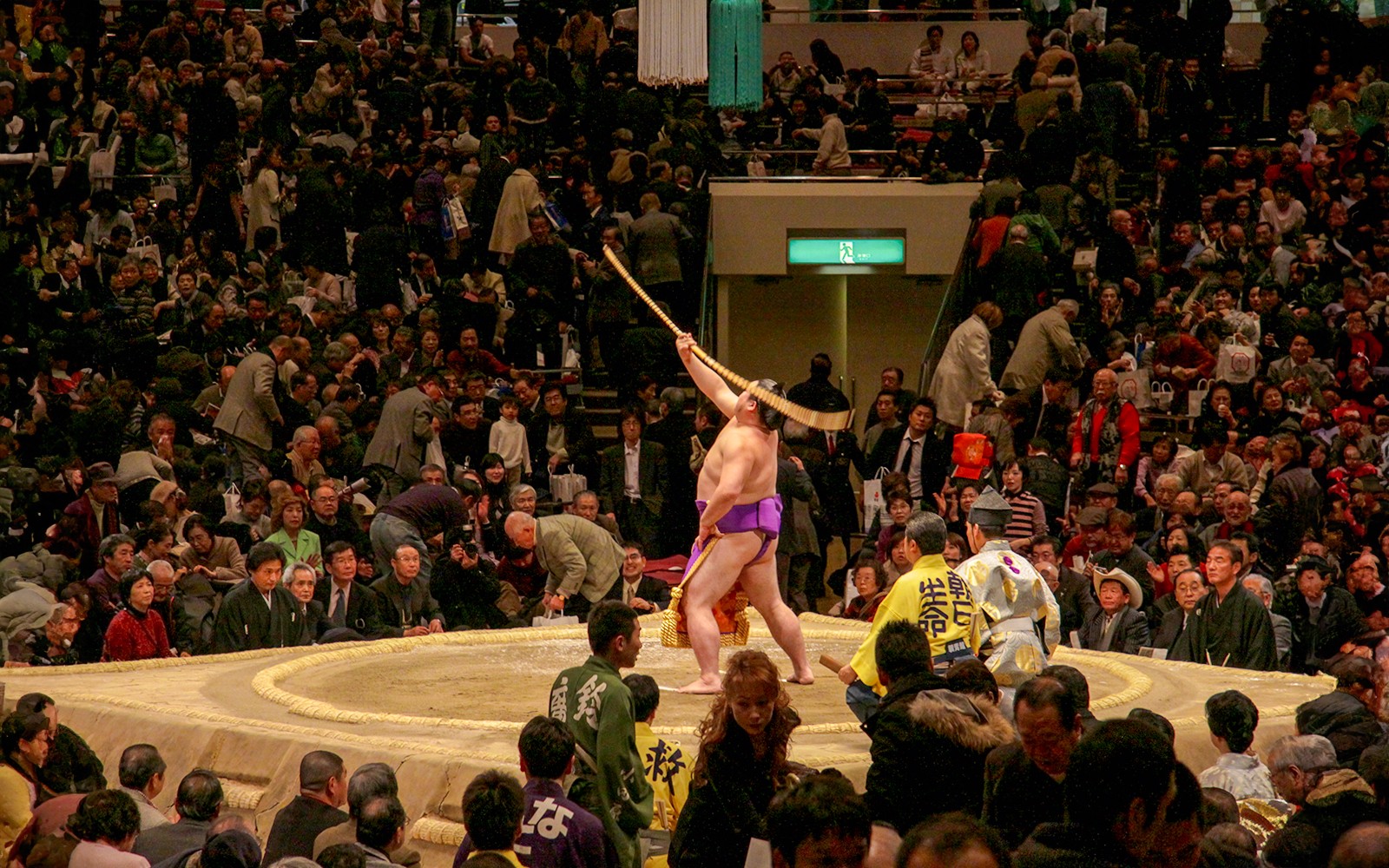 Sumo wrestler performing ritual at Fukuoka tournament with audience watching.