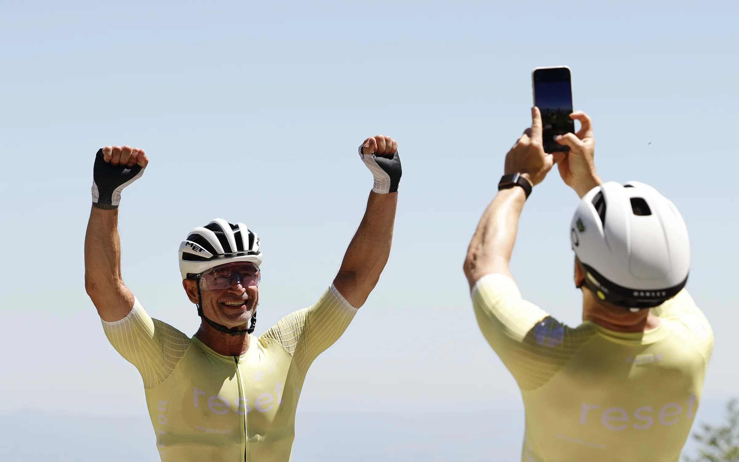 A reset cc rider celebrating with both fists raised at the Girona camp while a teammate films him