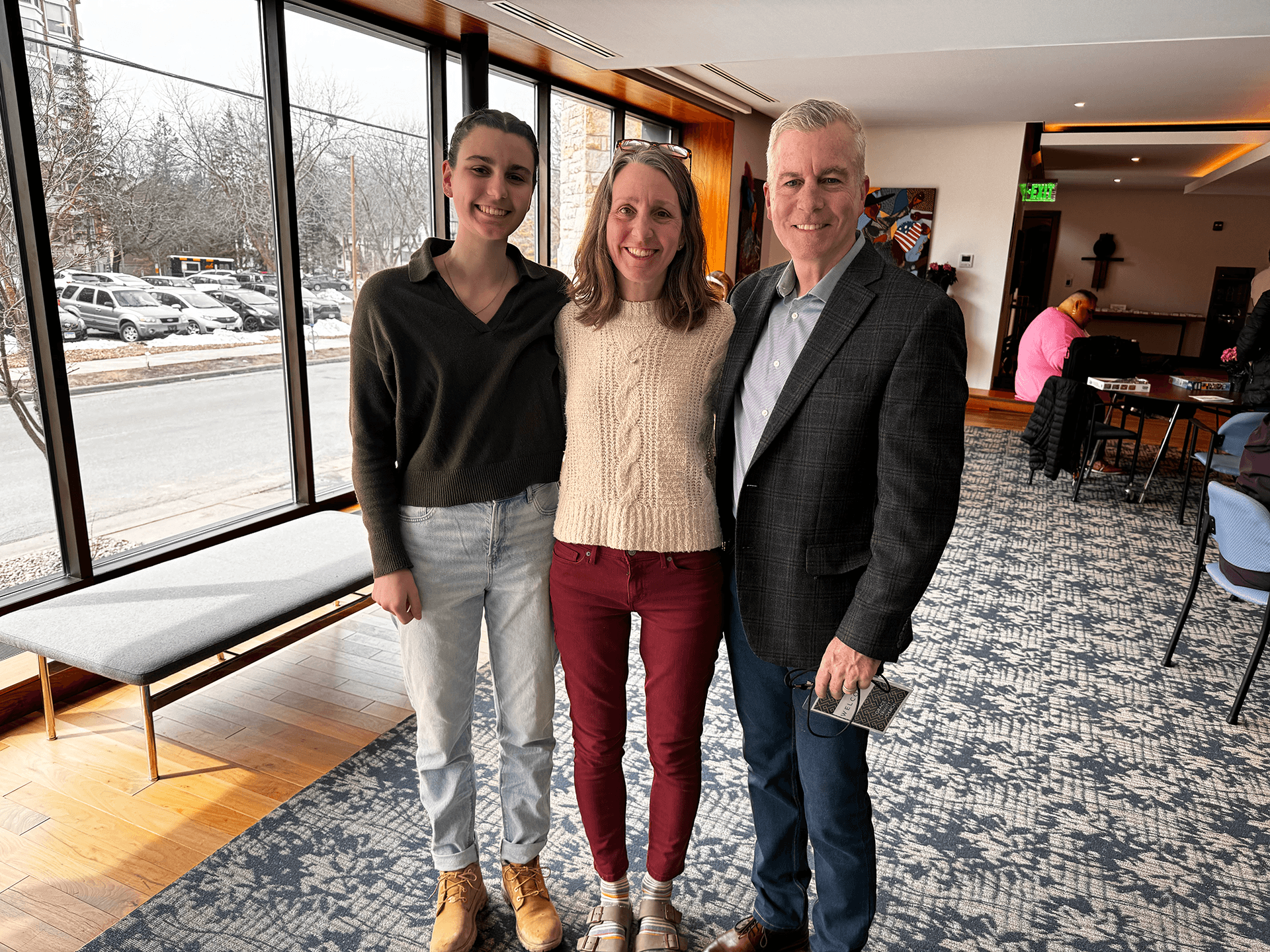 Two women and a man posing for a photo in the Grace Trinity Church lobby with large windows and natural light.