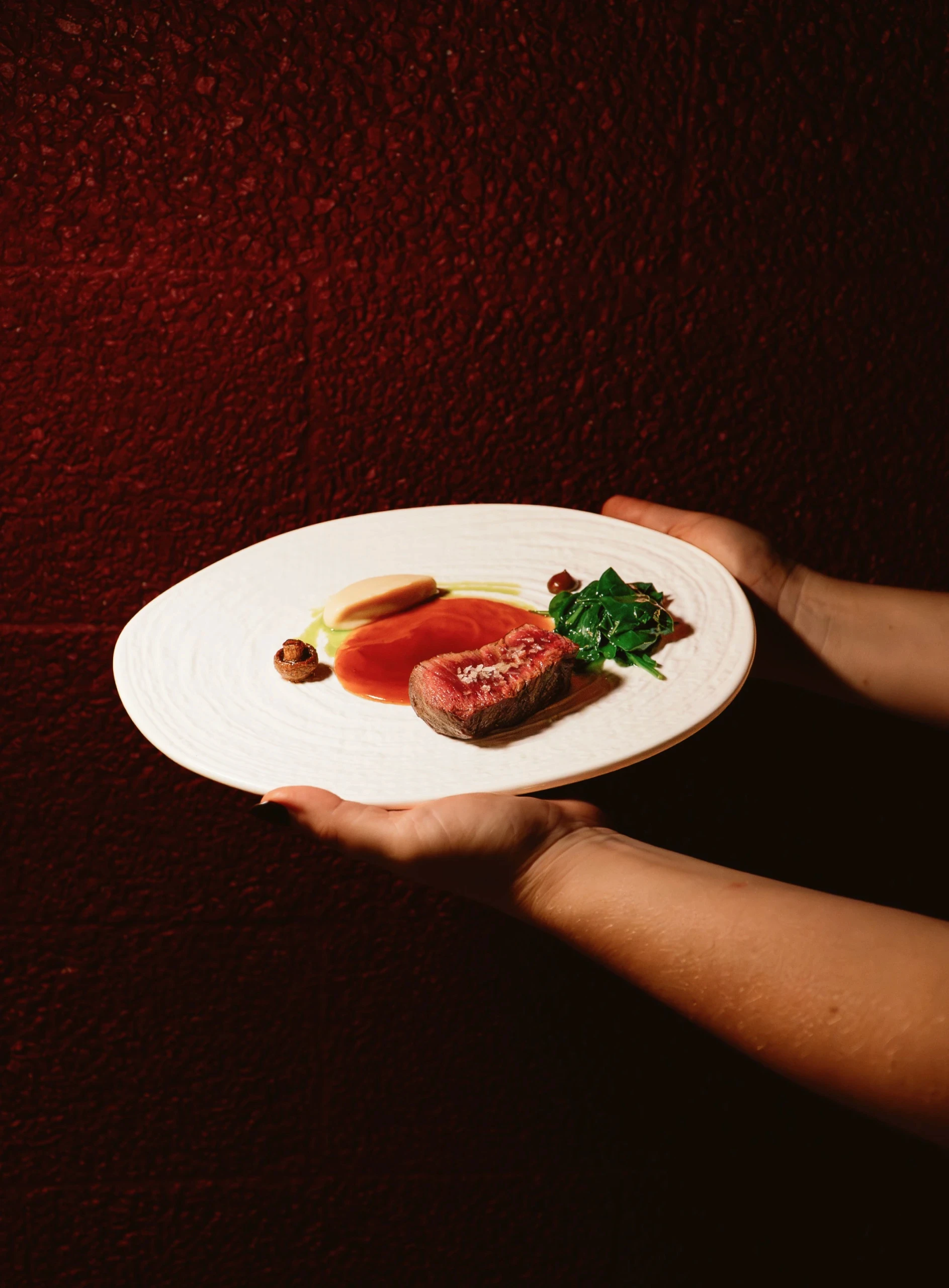 Manos sirviendo un plato de carne sobre fondo rojo, restaurante Atea