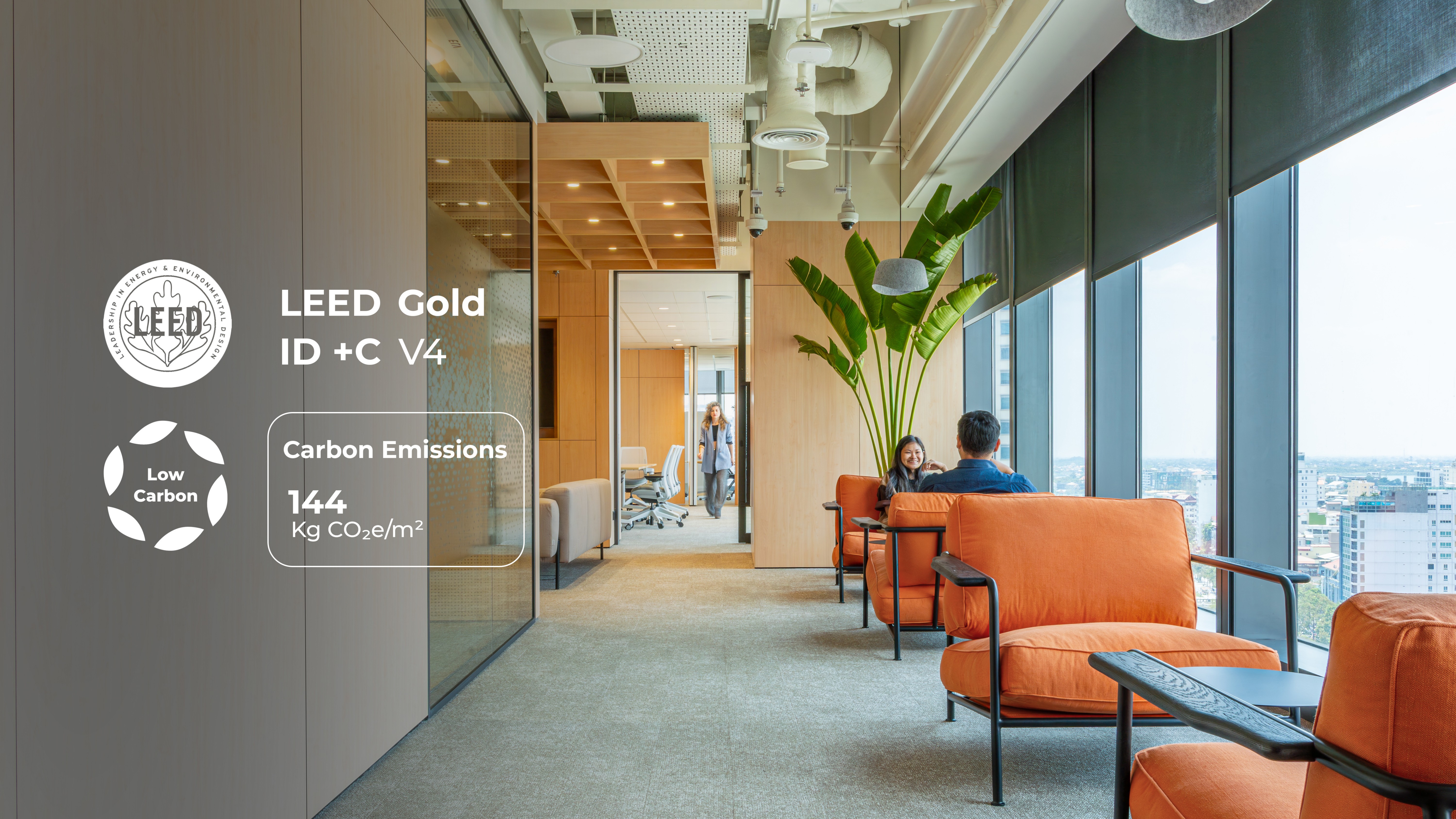 LEED Gold ID+C V4 certified office interior in Phnom Penh with low-carbon rating of 144 kg CO2e per square metre, featuring timber-lined partitions, exposed services ceiling, biophilic planting, and orange lounge seating with city views supporting occupant wellbeing and operational efficiency