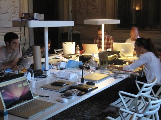 A photo of a group of people sitting around a table and working on their laptops.
