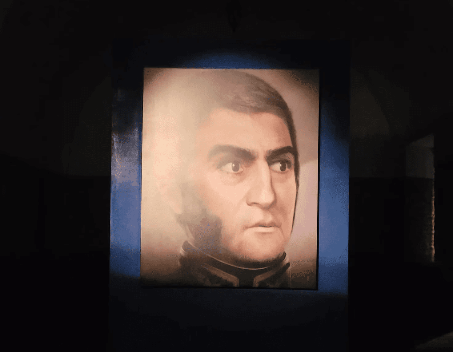 Retrato iluminado de San Martín expuesto en una sala oscura del museo.